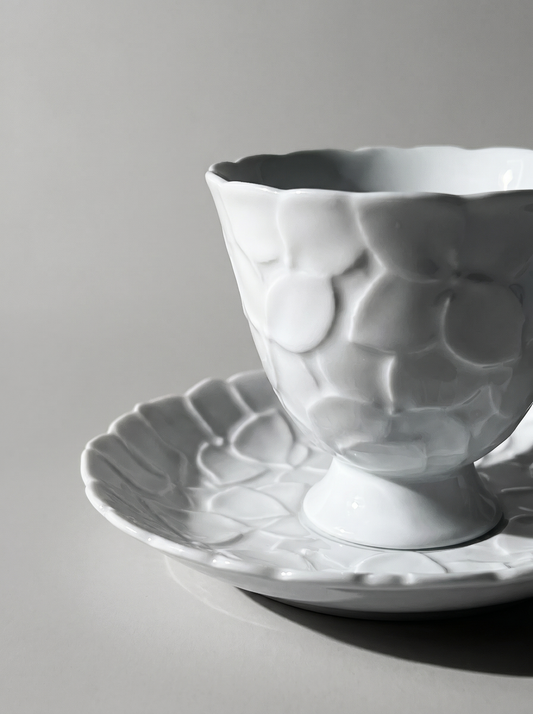 close up of Japanese white koransha teacup with a short handle and a saucer on a sodt grey background