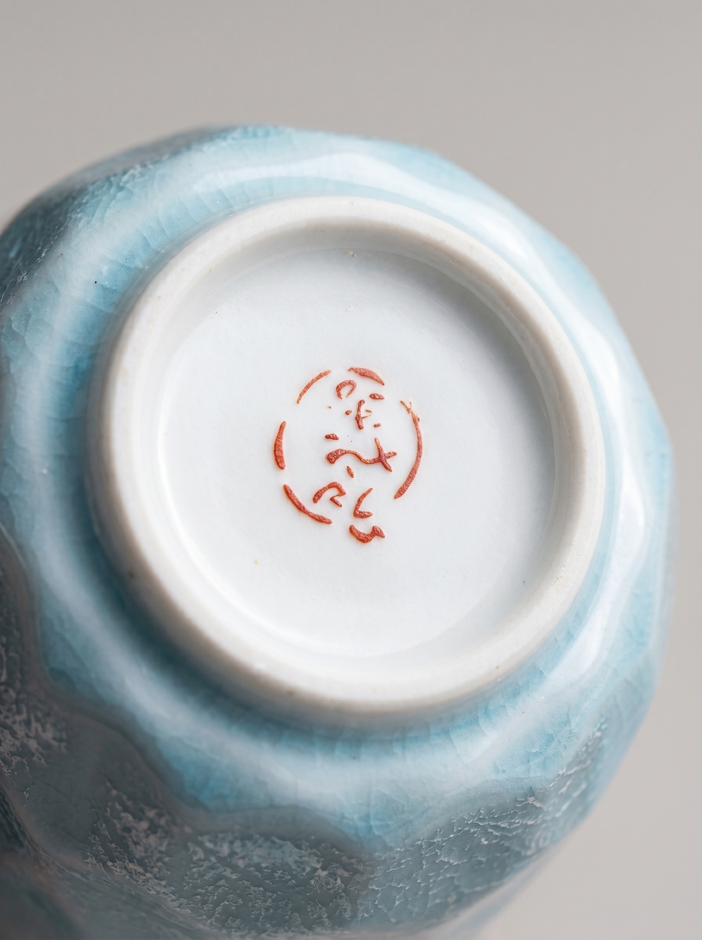 Ceramic cup with a blue glaze and red Japanese stamp on a gray background