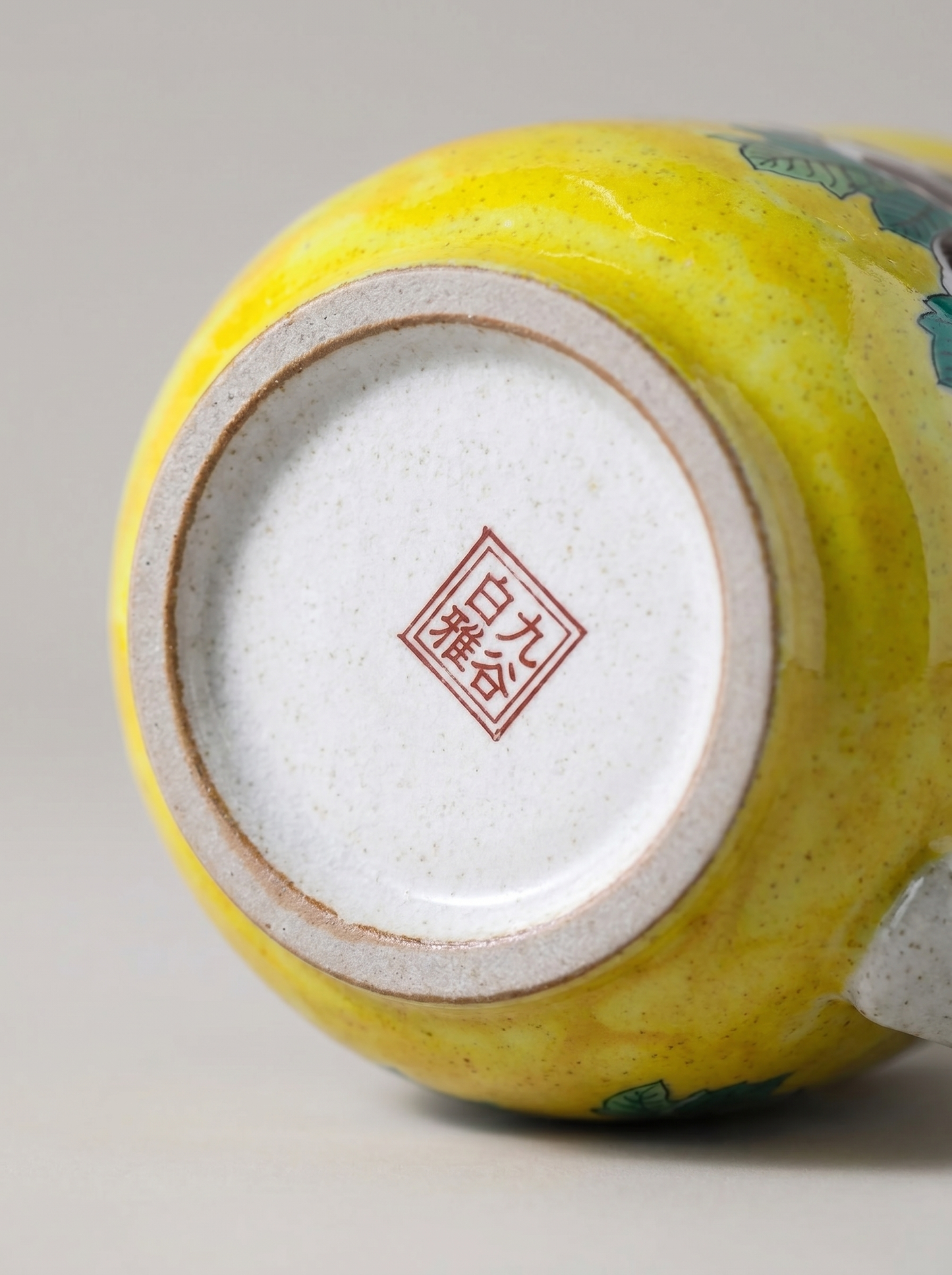 Close-up of a yellow ceramic cup with a visible brand logo on a gray background