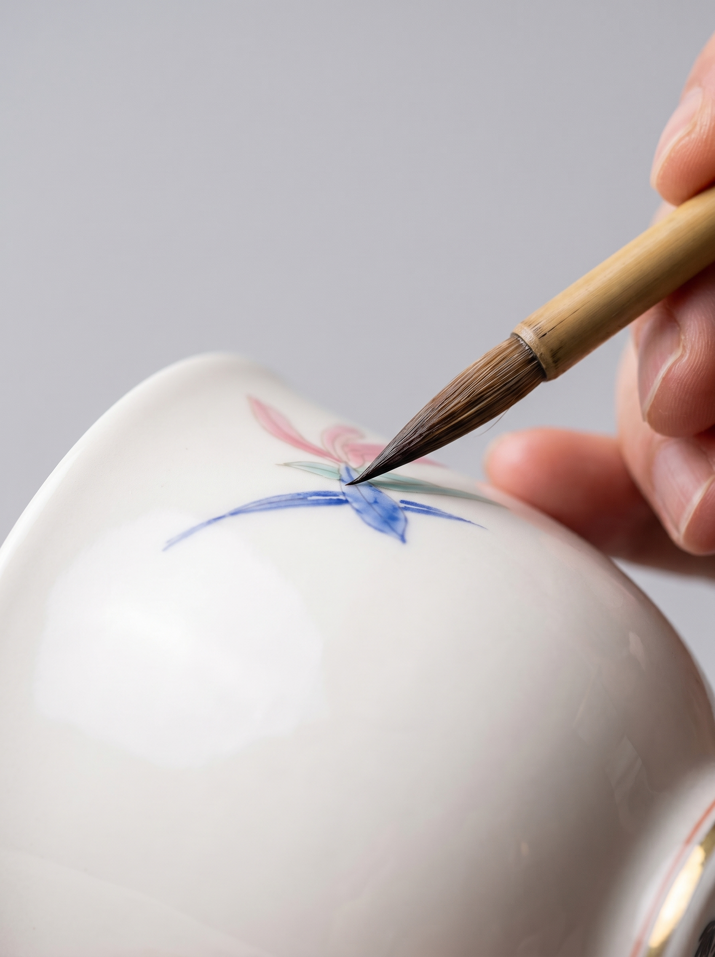 Person painting wild orchids on a white porcelain teacup with a brush