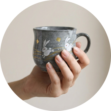 Hand holding a ceramic mug with rabbit and golden moon design on a beige background