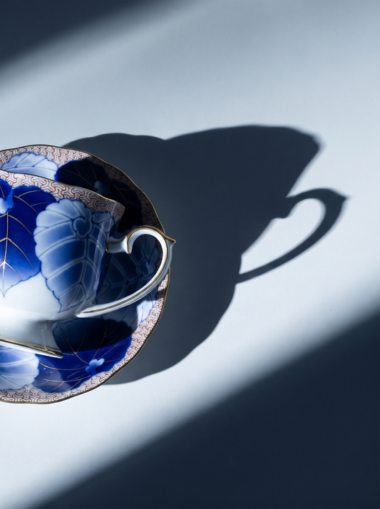 Blue and white ceramic teacup and saucer casting a shadow on a light blue background