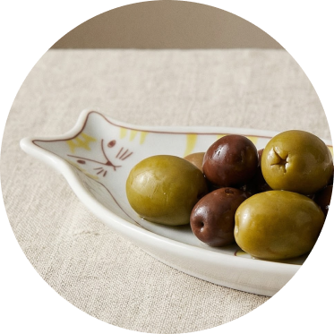 Assorted olives in a decorative Japanese cat-shaped ceramic plate on a linen surface
