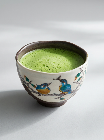 Ceramic bowl with green tea and decorative birds on a white background