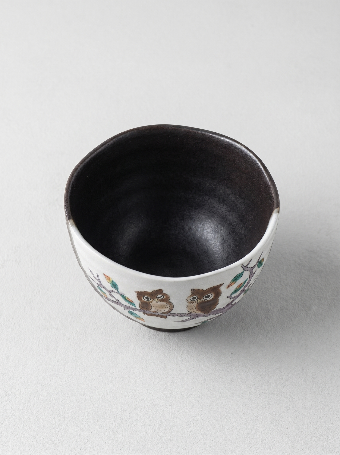 Japanese ceramic cup with owl design on a light gray background top view