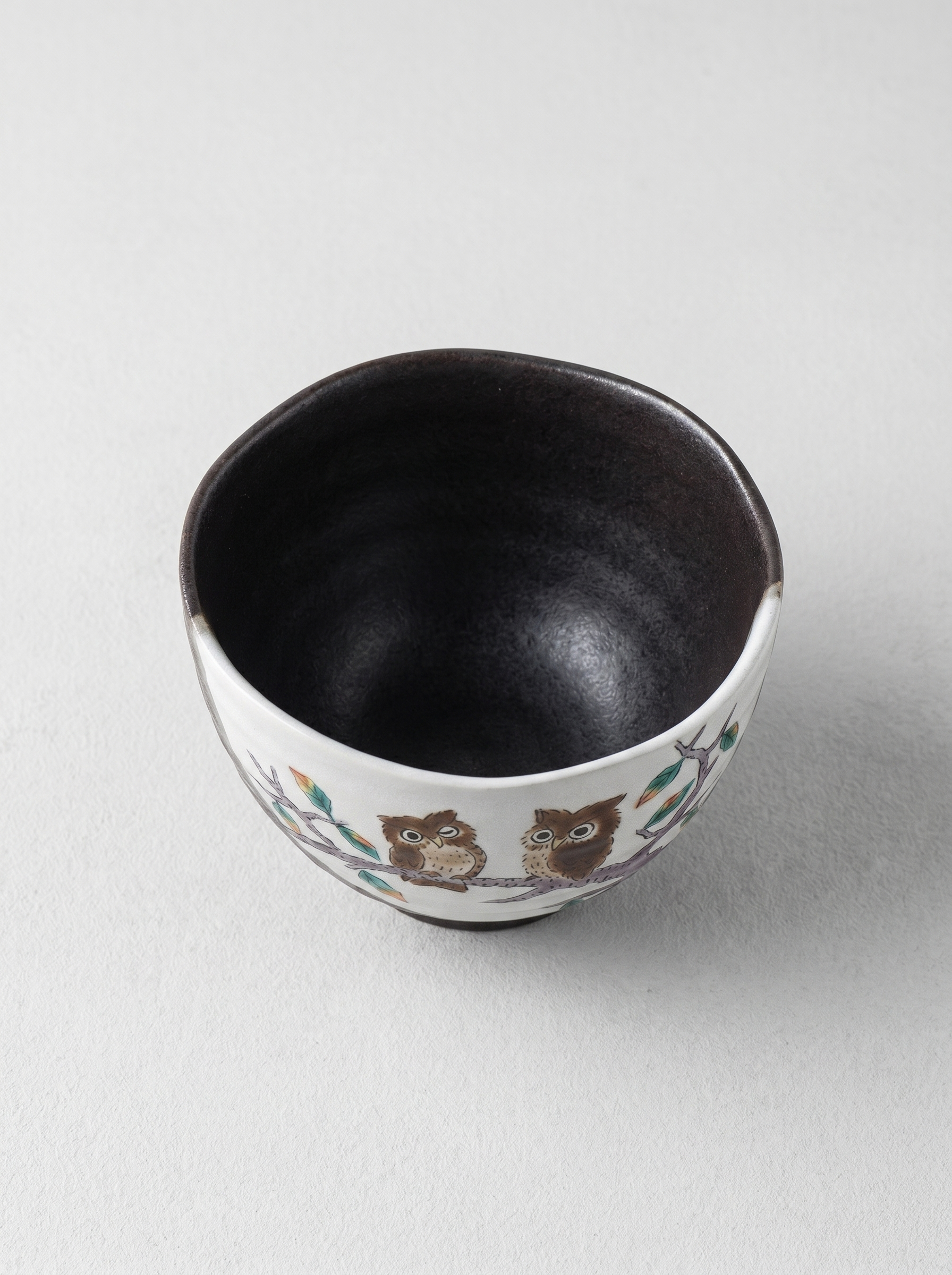 Japanese ceramic cup with owl design on a light gray background top view