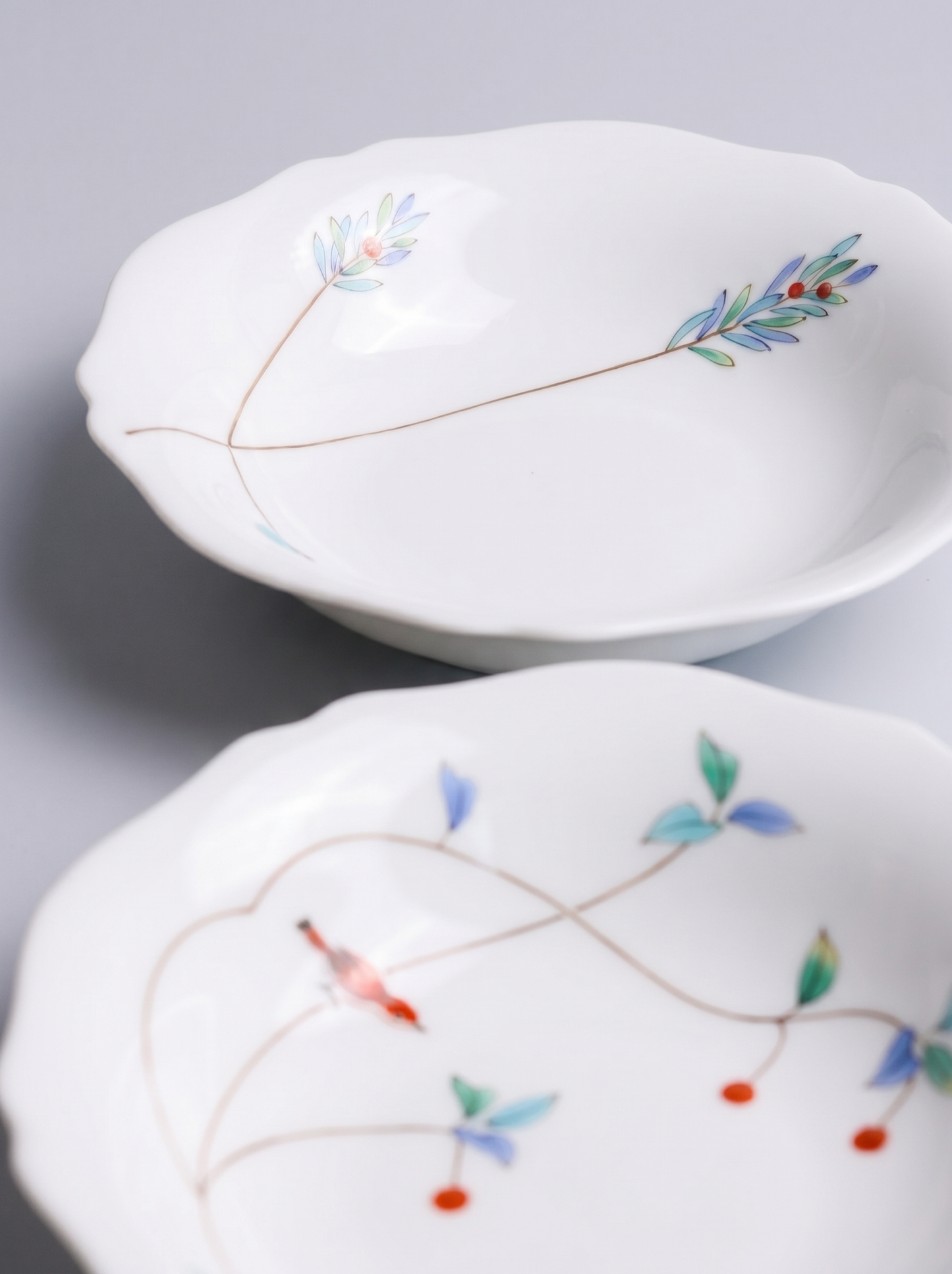 Two white japanese koransha porcelain bowls with floral patterns on a light gray background