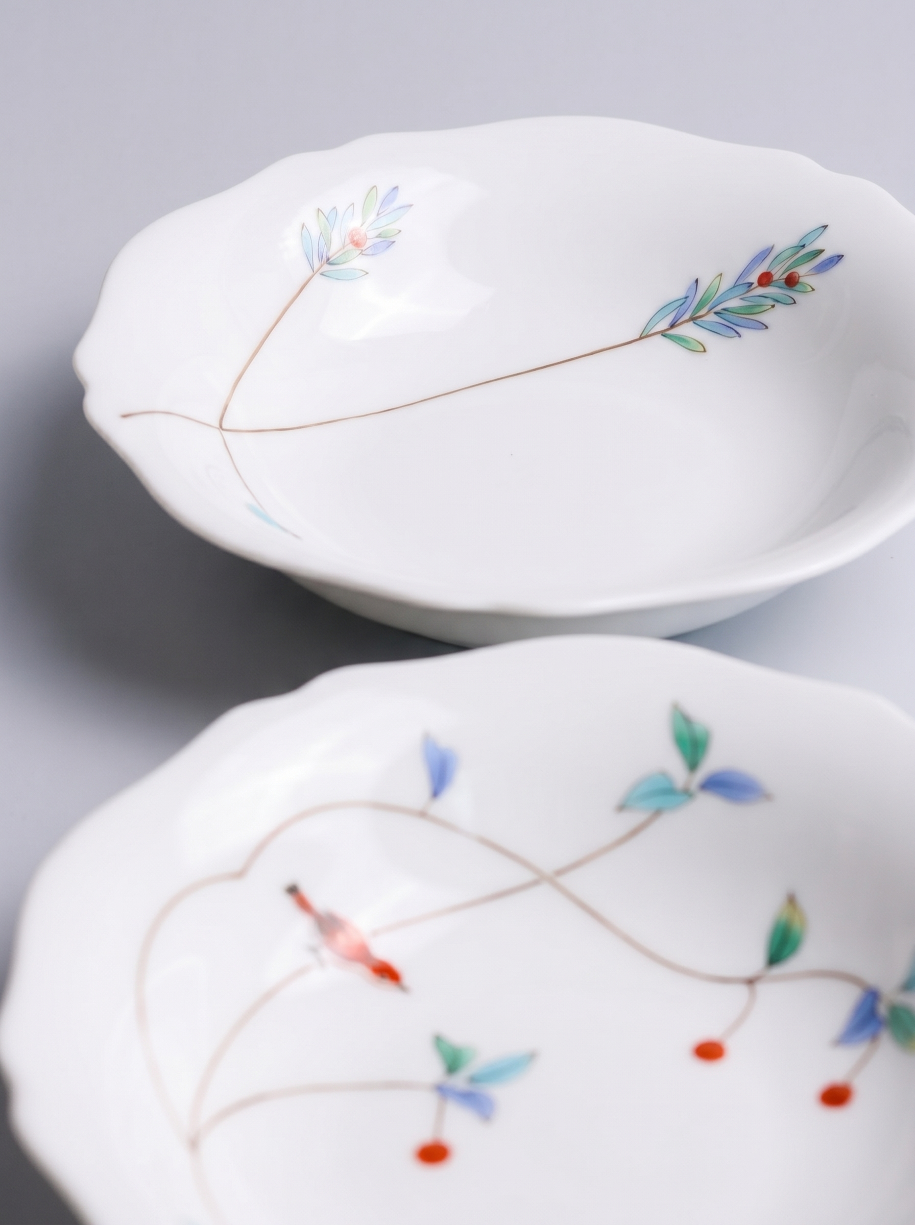 Two white japanese koransha porcelain bowls with floral patterns on a light gray background