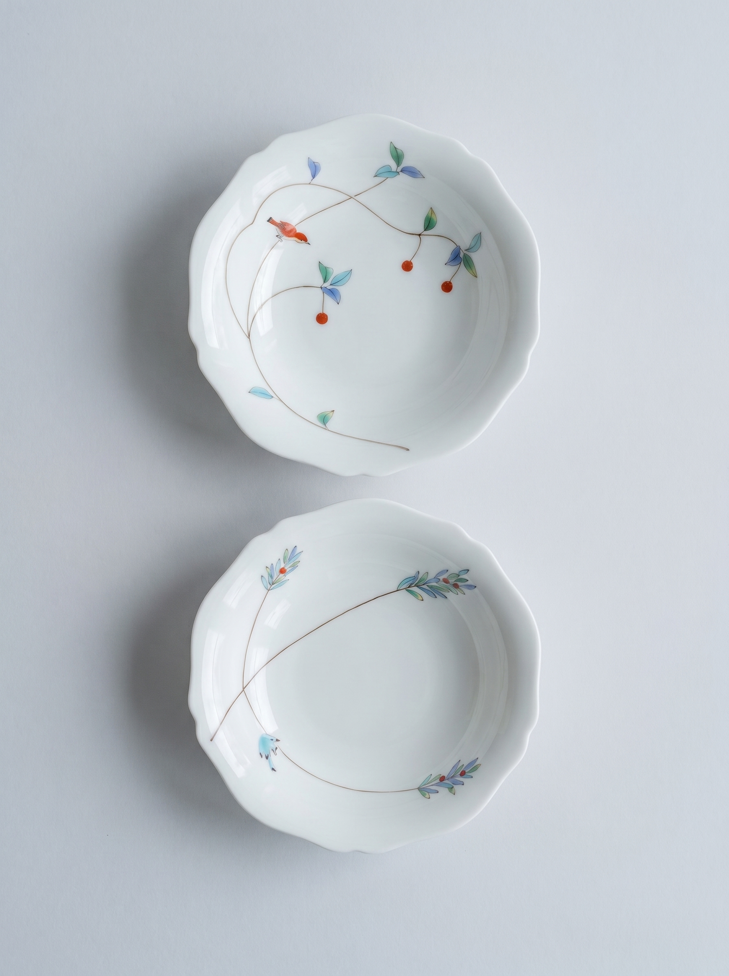 Two white japanese koransha porcelain bowls with floral patterns on a light gray background