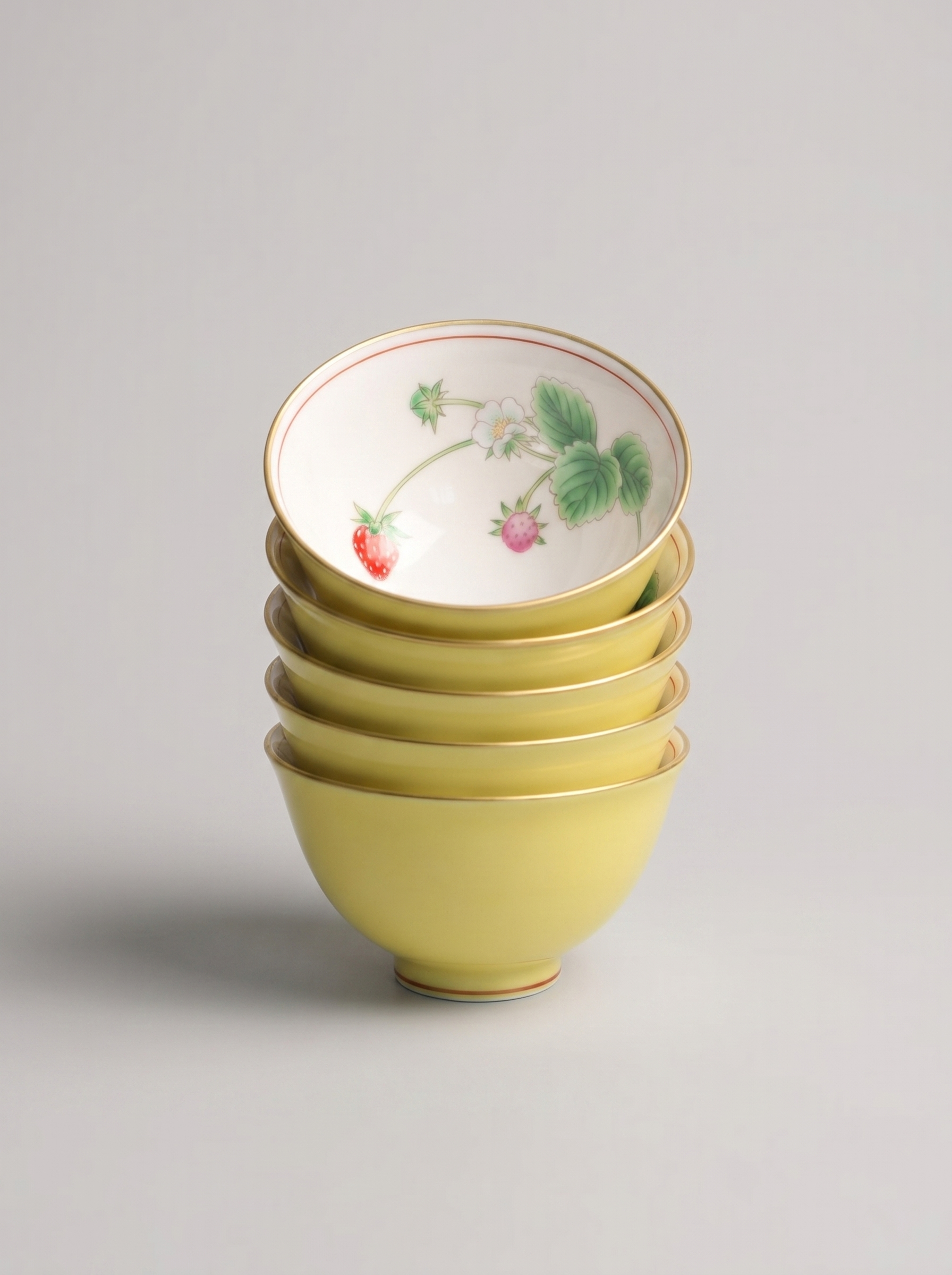 Stack of five yellow Japanese porcelain small teacups in yellow color with berry design on a gray background