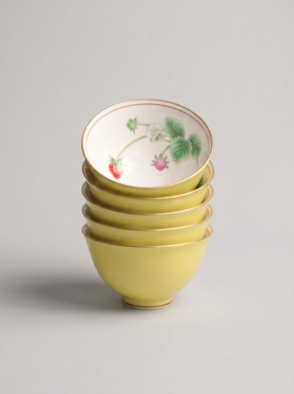 Stack of five yellow Japanese porcelain small teacups in yellow color with berry design on a gray background