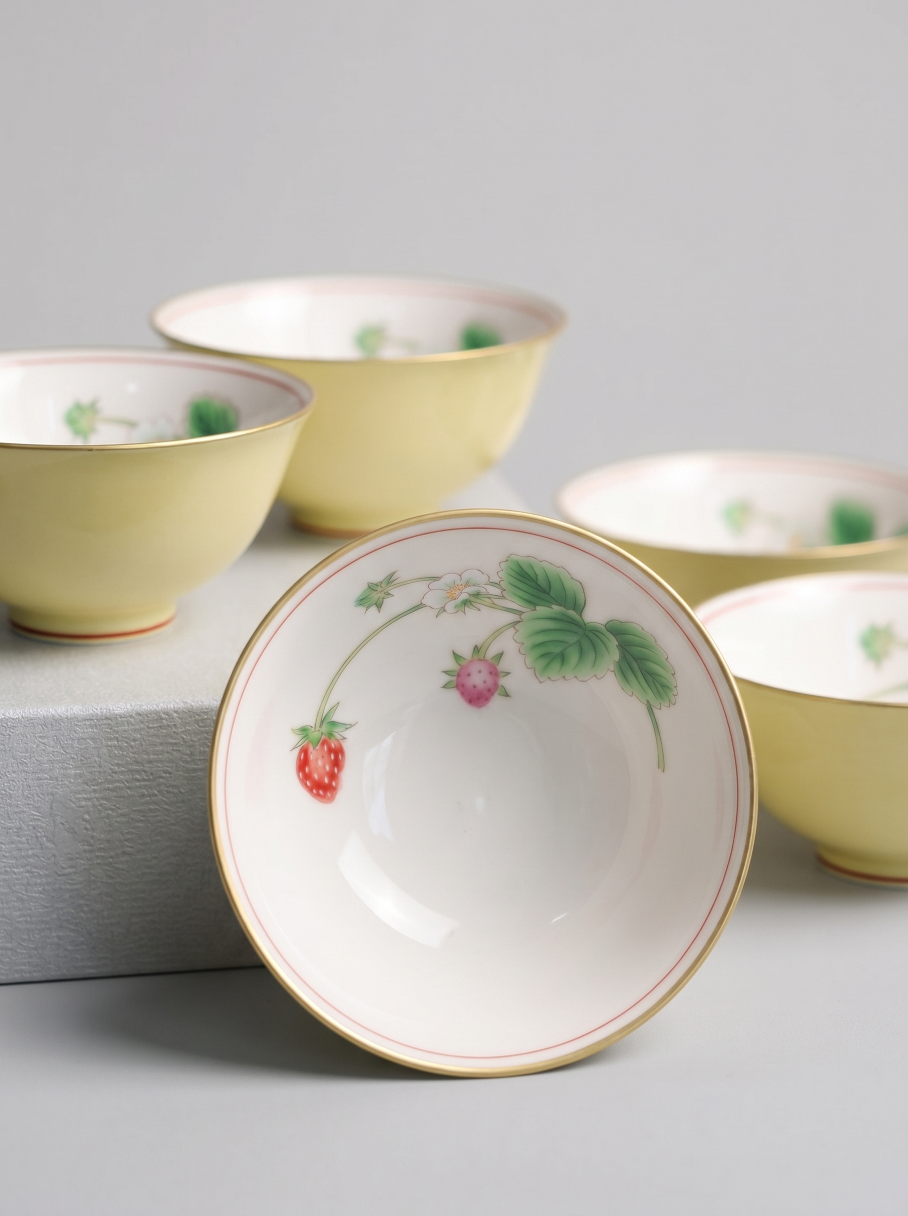 Close up of yellow porcelain teacup with berry designs on a gray background