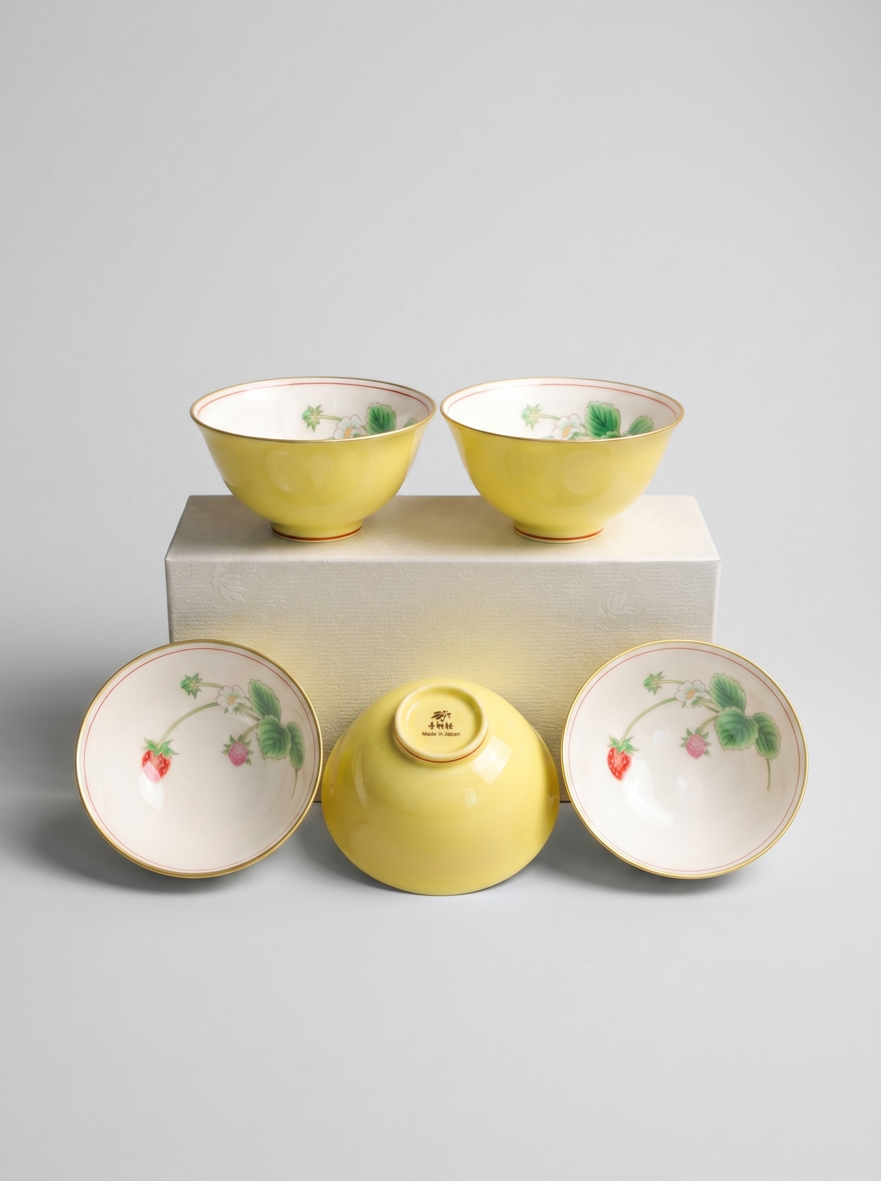 Set of five yellow Japanese koransha porcelain teacups with berry designs on a gray background