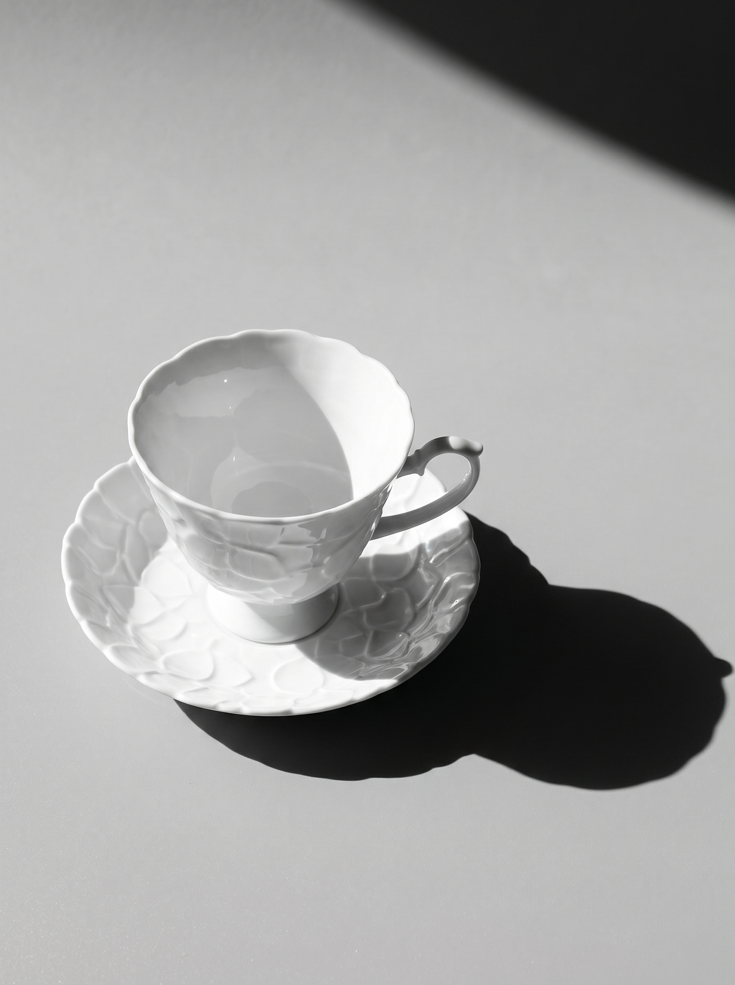 side view of Japanese white koransha teacup with a short handle and a saucer on a sodt grey background, showcasing its embossed surface