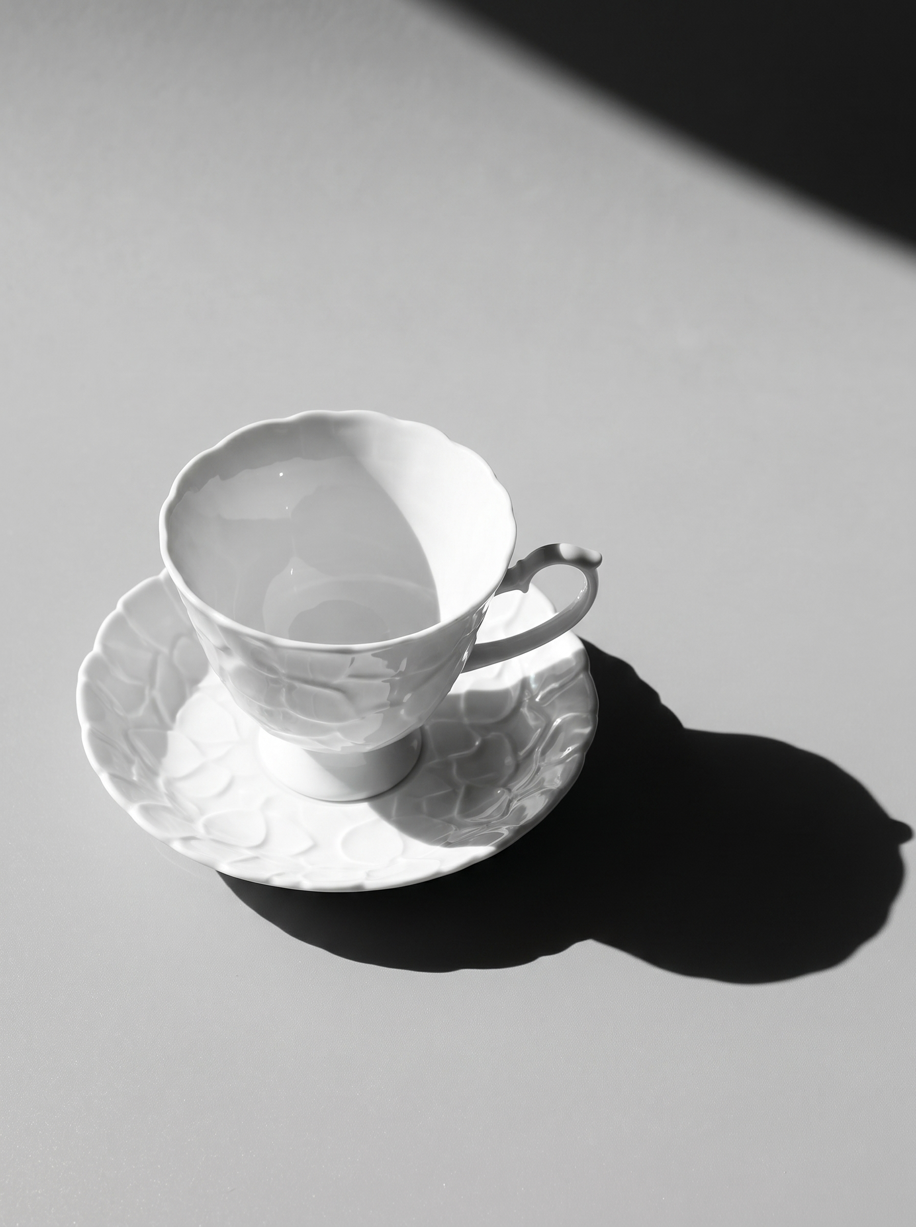 side view of Japanese white koransha teacup with a short handle and a saucer on a sodt grey background, showcasing its embossed surface