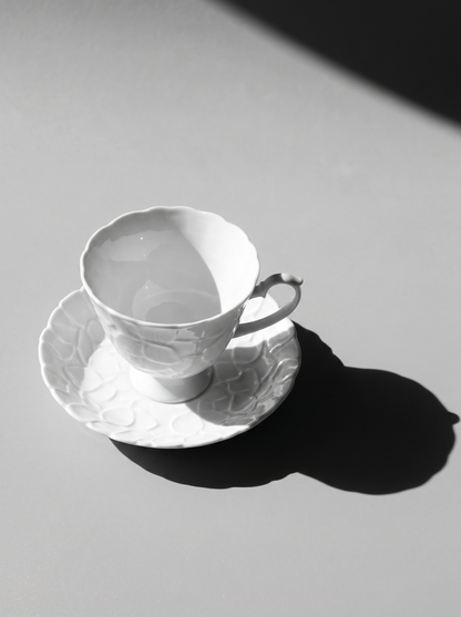 side view of Japanese white koransha teacup with a short handle and a saucer on a sodt grey background, showcasing its embossed surface