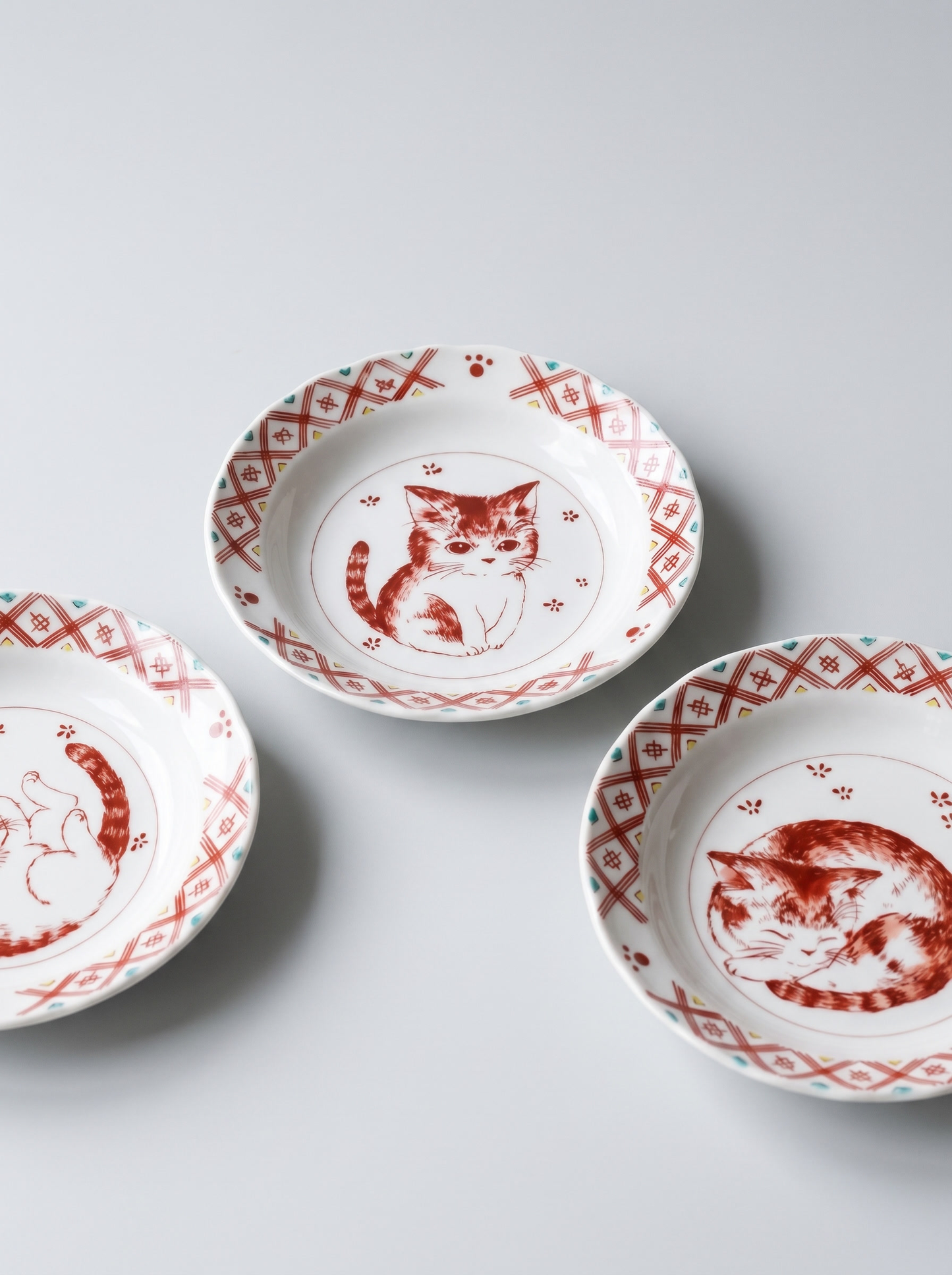 Three ceramic plates with red cat illustrations on a light gray background