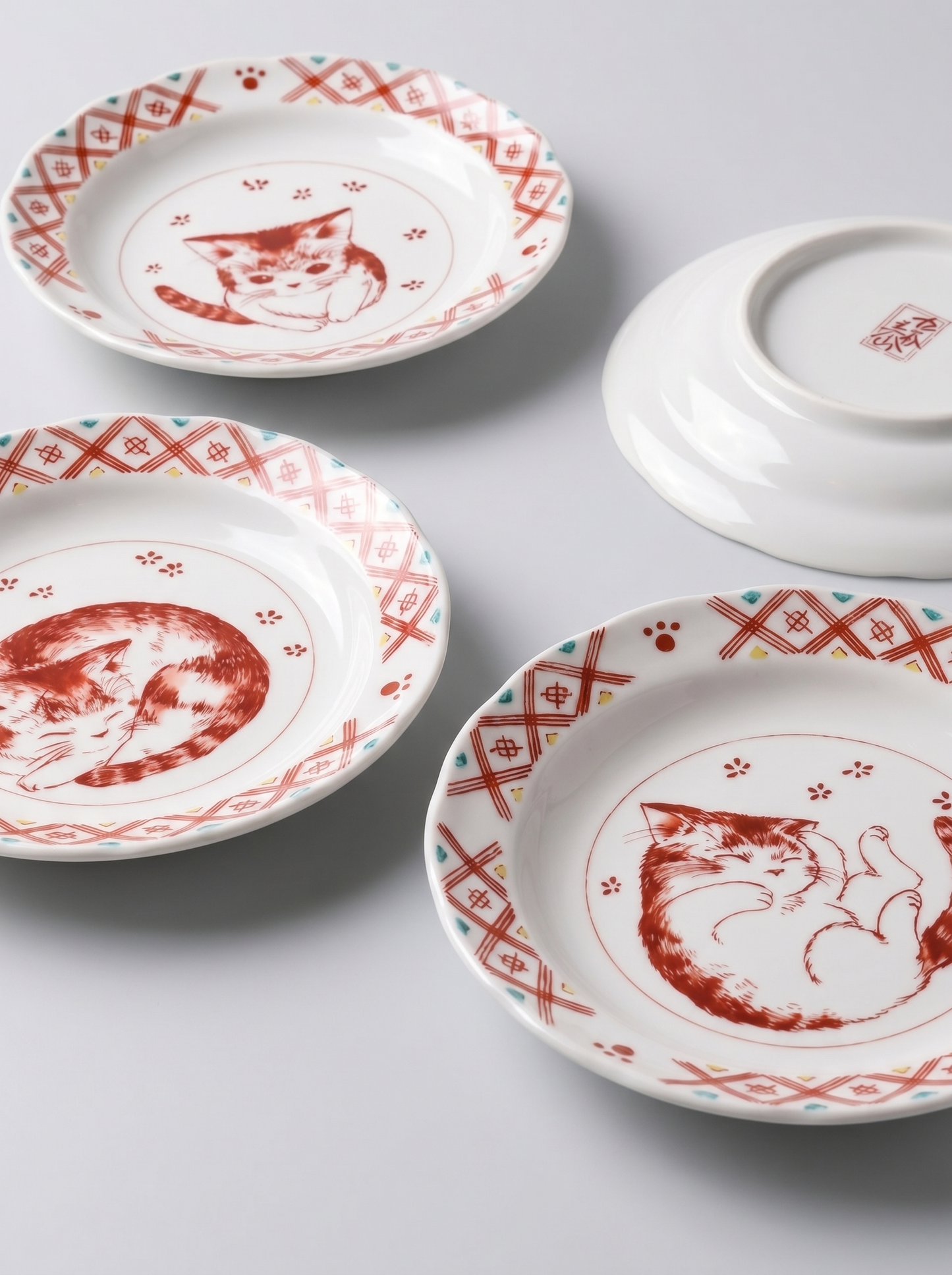 Set of japanese ceramic plates with red cat illustrations on a light gray background