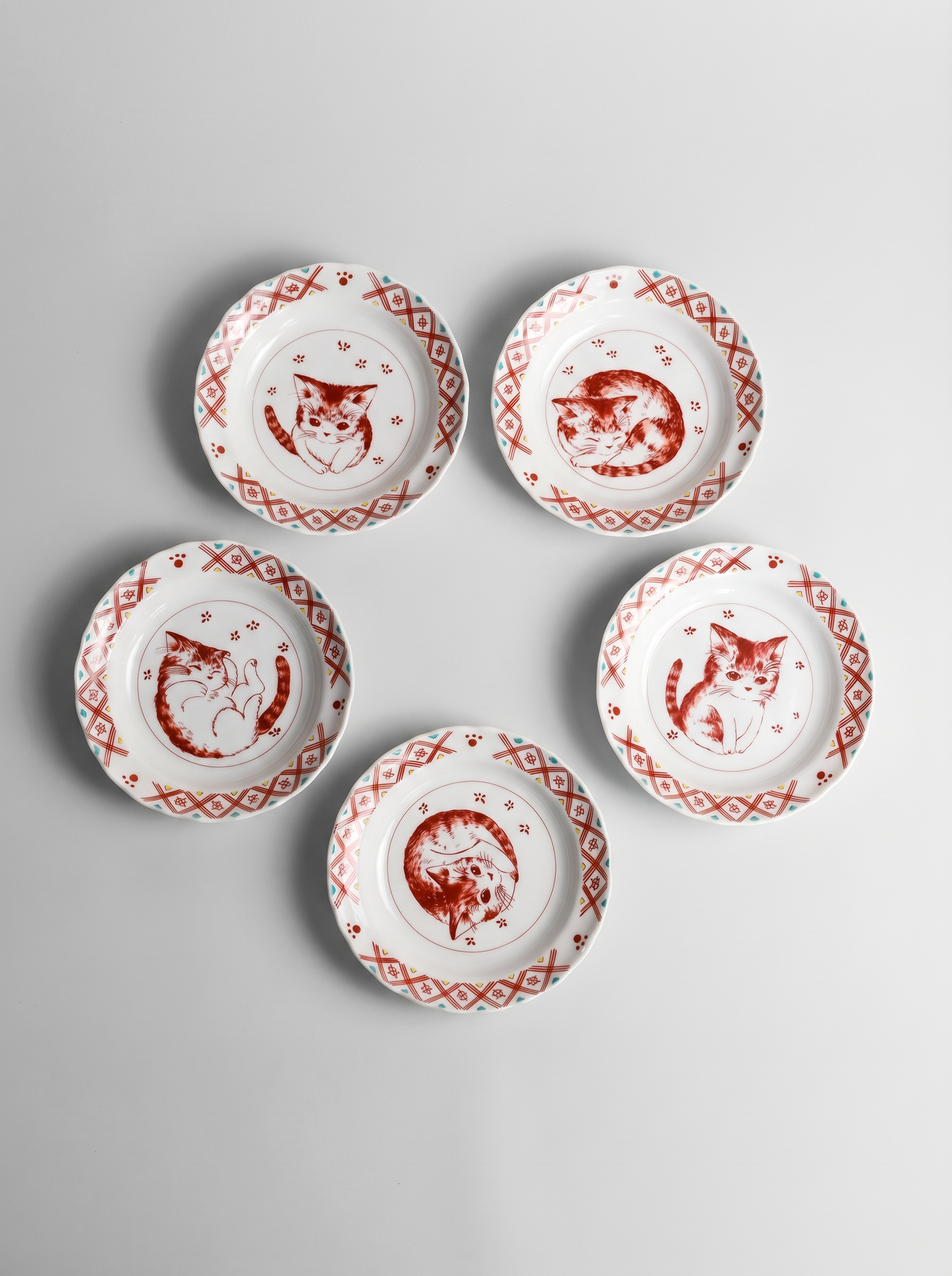 Set of five small white plates with red cat illustrations on a gray background