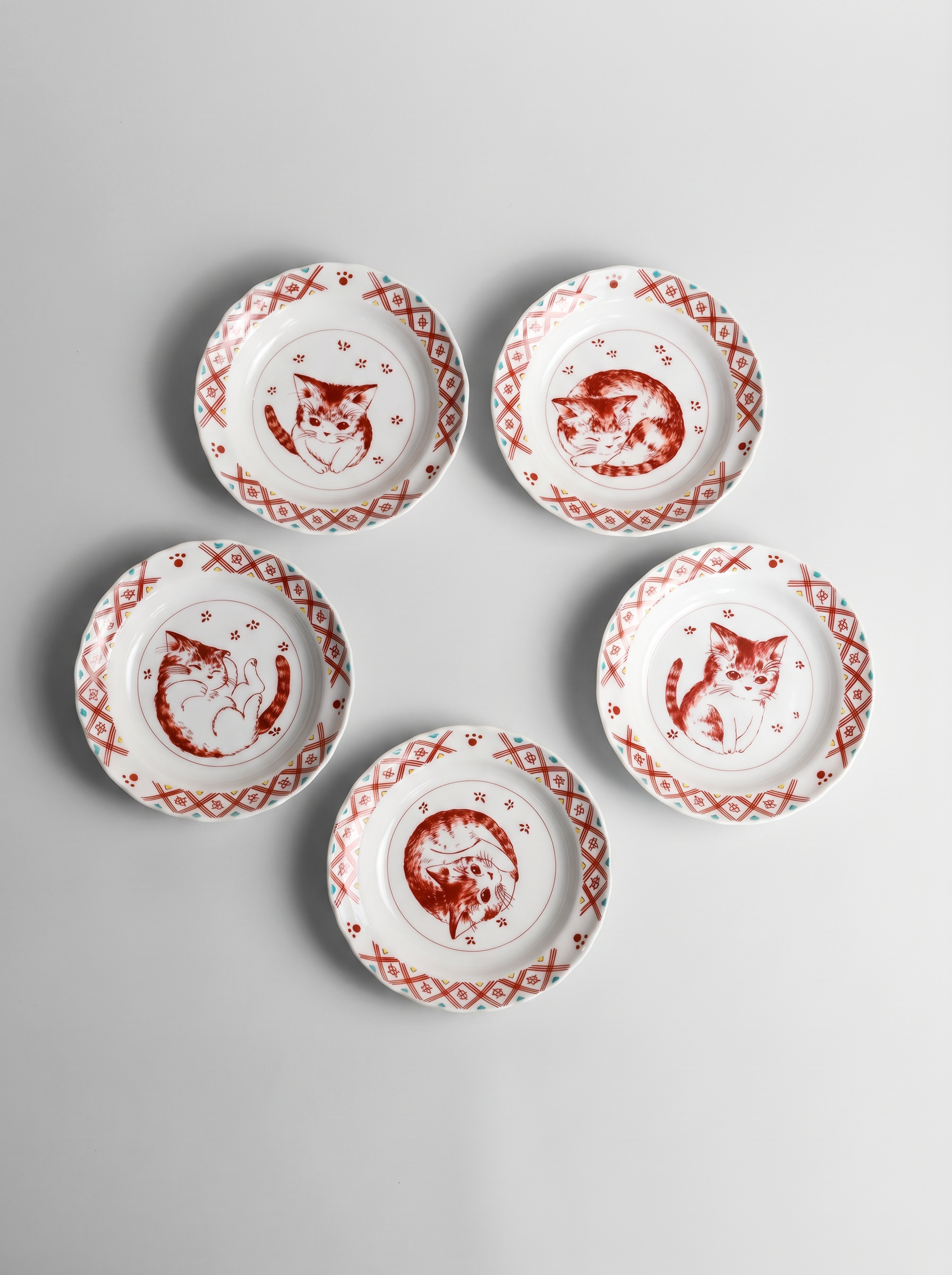 Set of five small white plates with red cat illustrations on a gray background