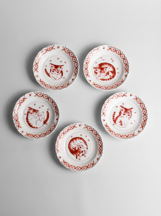 Set of five small white plates with red cat illustrations on a gray background