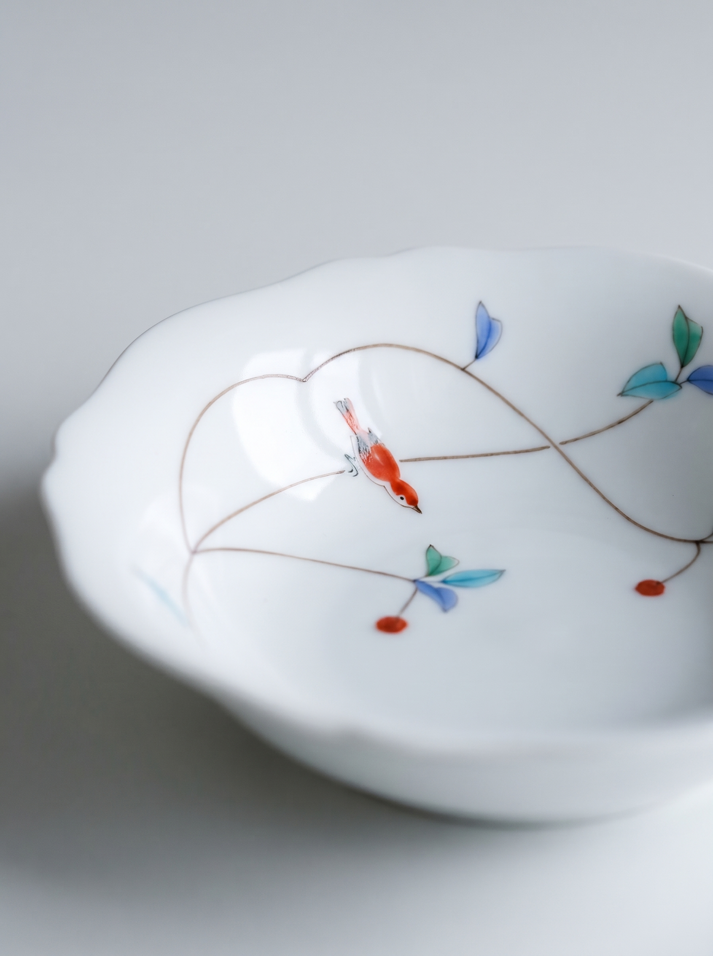 Close up of white japanese koransha porcelain bowl with floral patterns on a light gray background showcasing bird on a branch hand-painted illustration