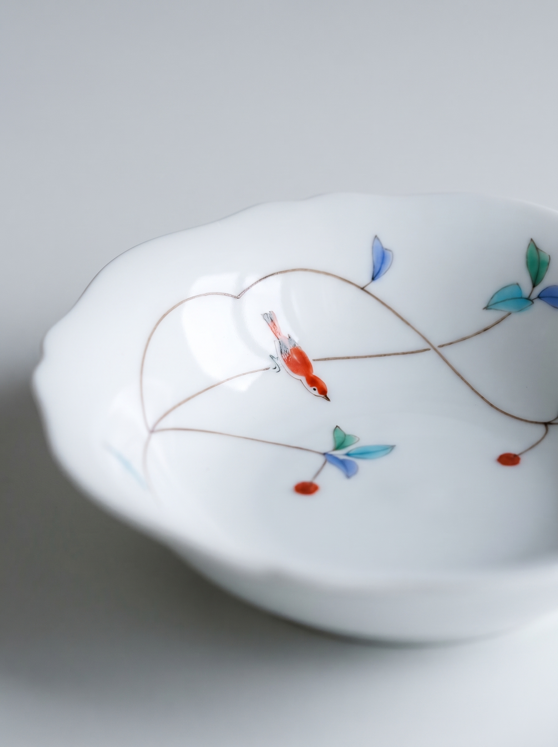 Close up of white japanese koransha porcelain bowl with floral patterns on a light gray background showcasing bird on a branch hand-painted illustration