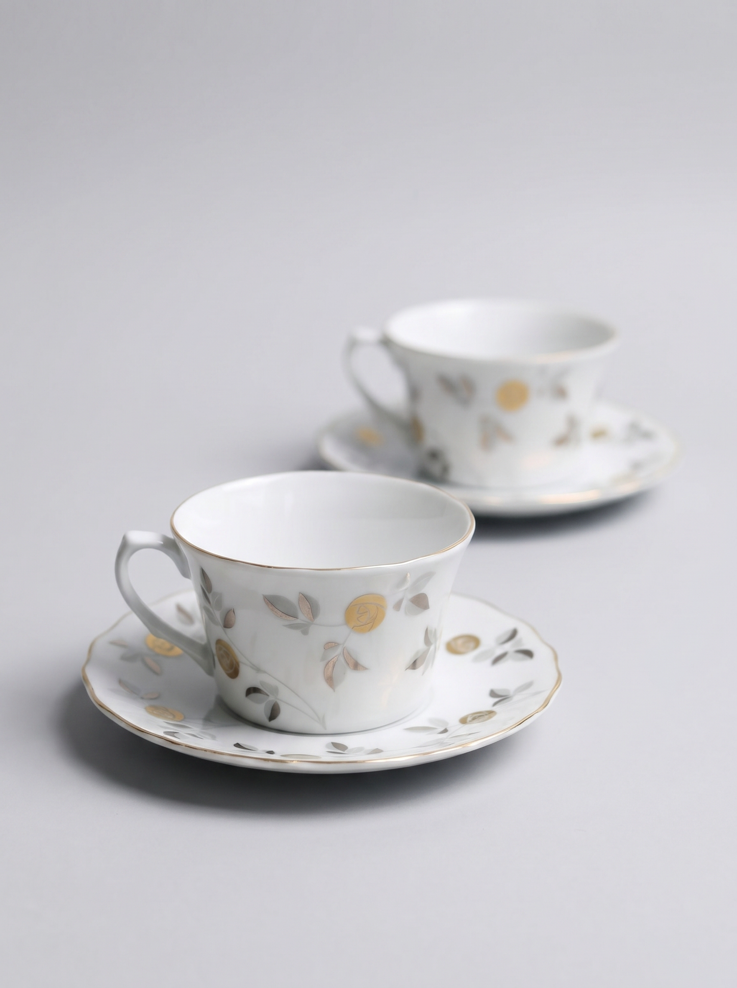 Two Japanese koransha porcelain tea cups with saucers and with gold and silver design on a light gray background