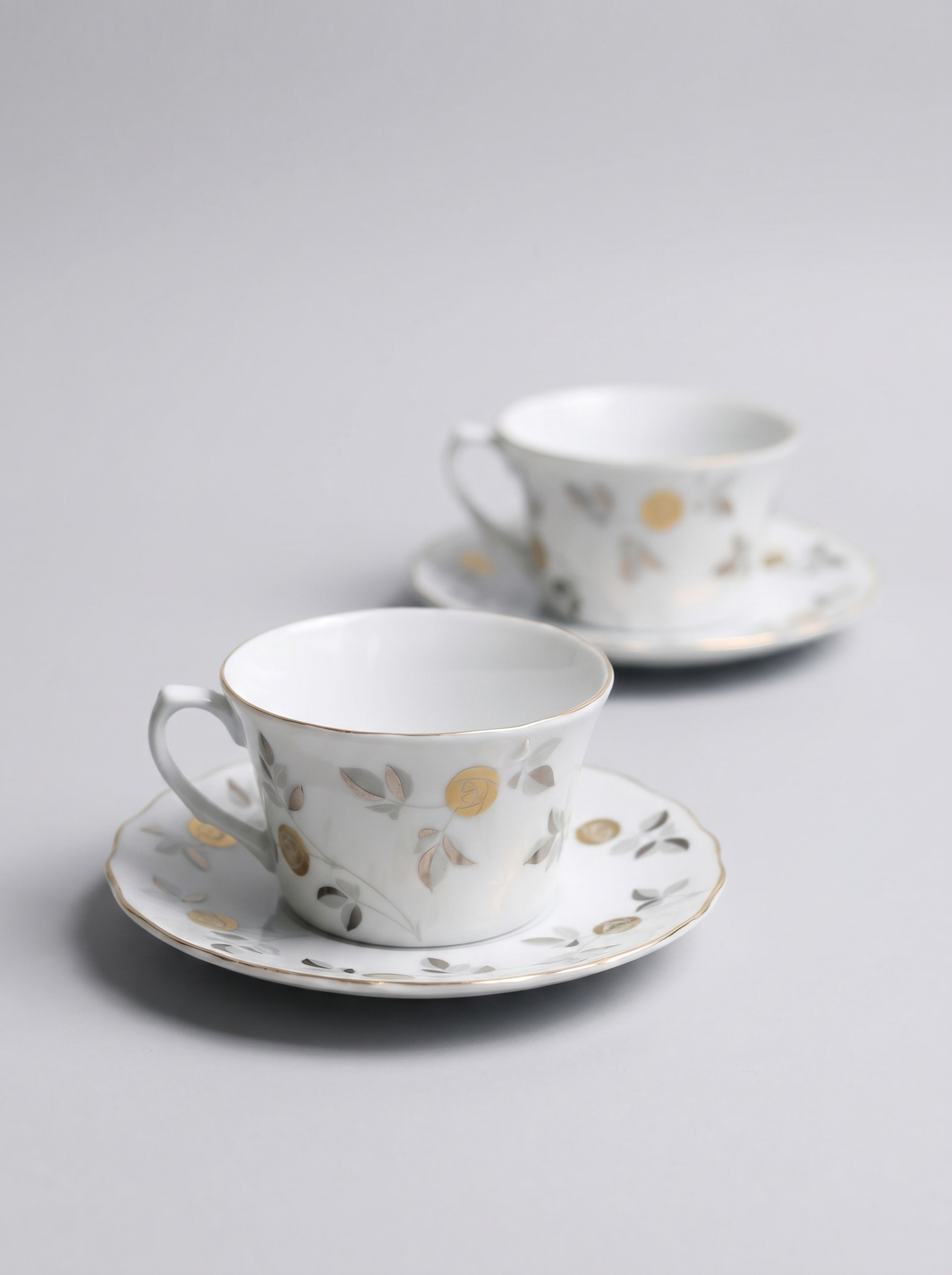 Two Japanese koransha porcelain tea cups with saucers and with gold and silver design on a light gray background