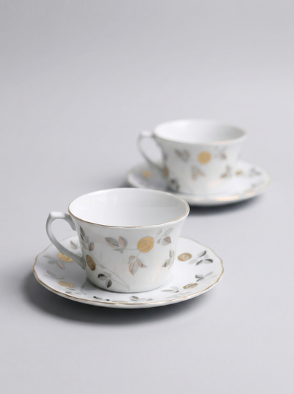 Two Japanese koransha porcelain tea cups with saucers and with gold and silver design on a light gray background