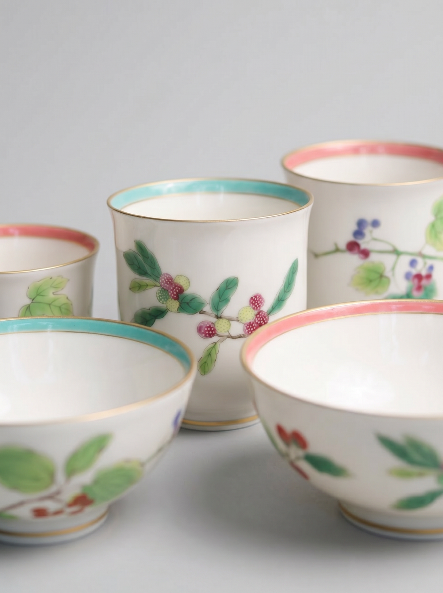 close up of set of four Japanese koransha porcelain cups with floral designs on a light gray background