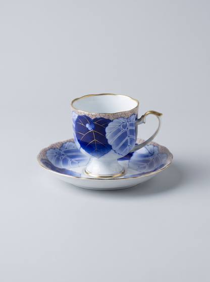 Ceramic cup and saucer with blue leaf design on a light gray background