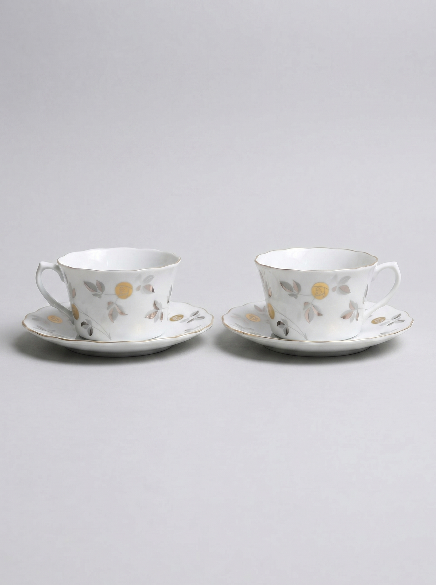 Two Japanese koransha porcelain tea cups with saucers and with gold and silver design on a light gray background