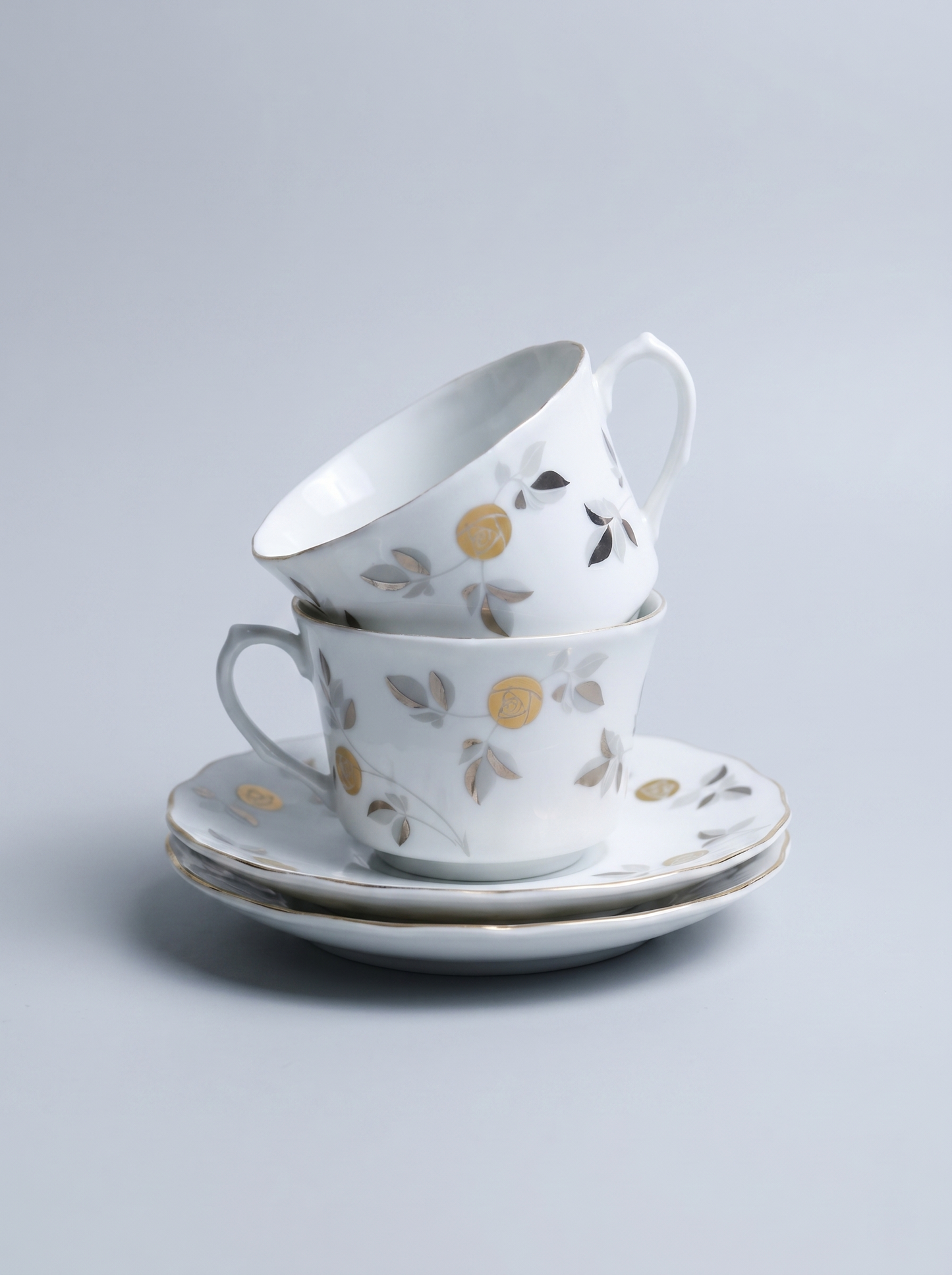 Set of ceramic cups and saucers with floral and geometric patterns on a light gray background