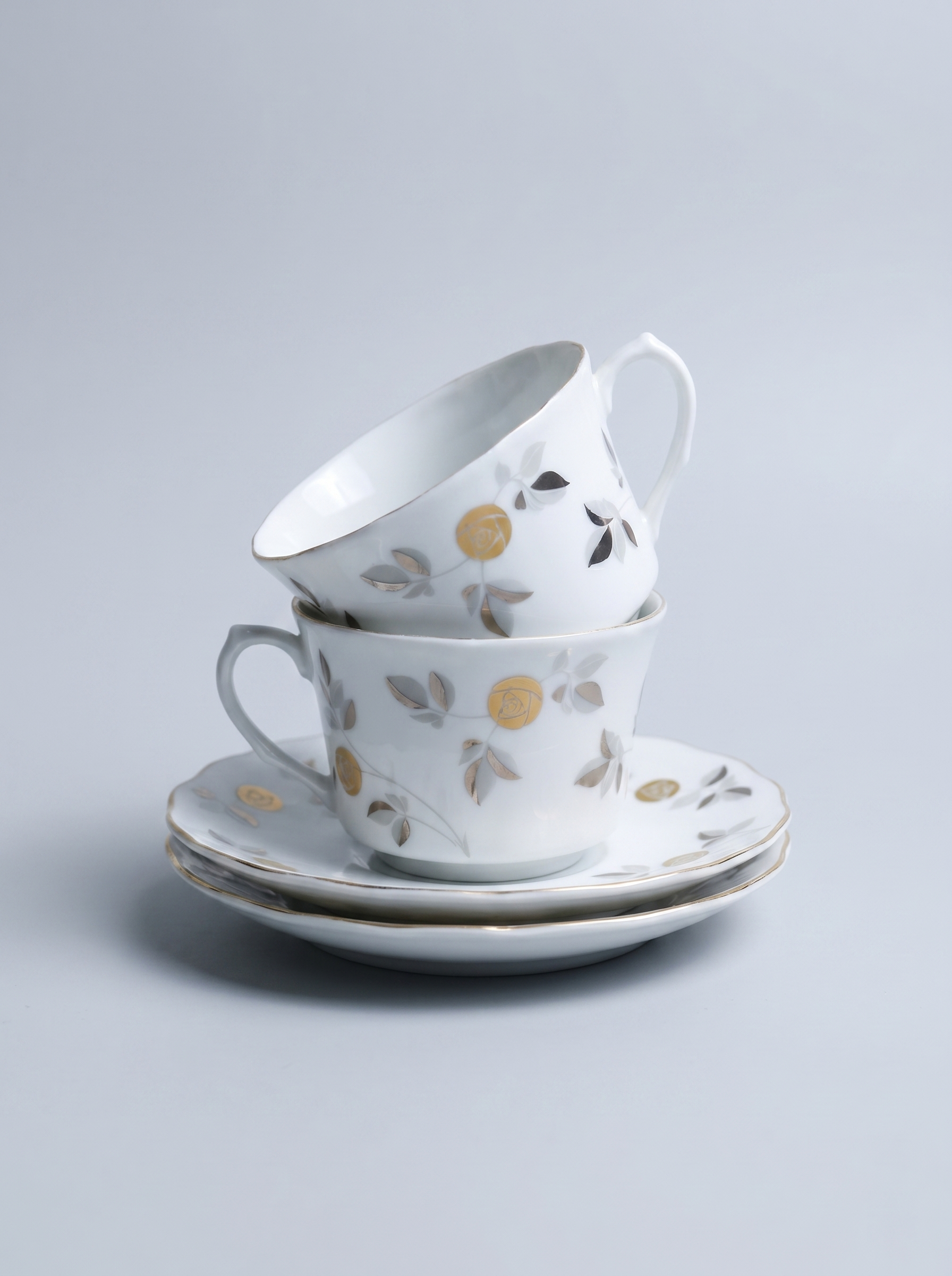 Set of ceramic cups and saucers with floral and geometric patterns on a light gray background