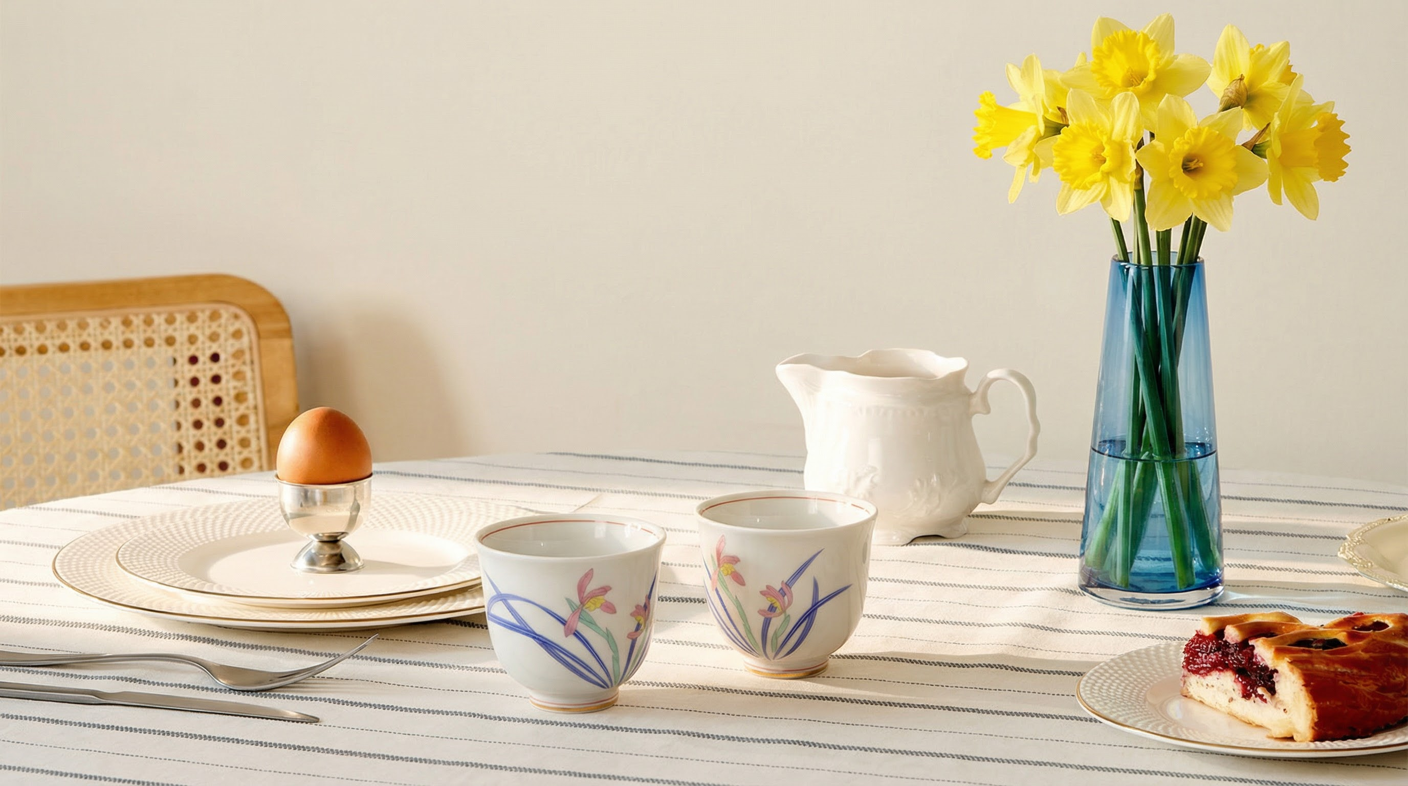 Café setting with two cups, a pitcher, and a plate of cake on a wooden table.