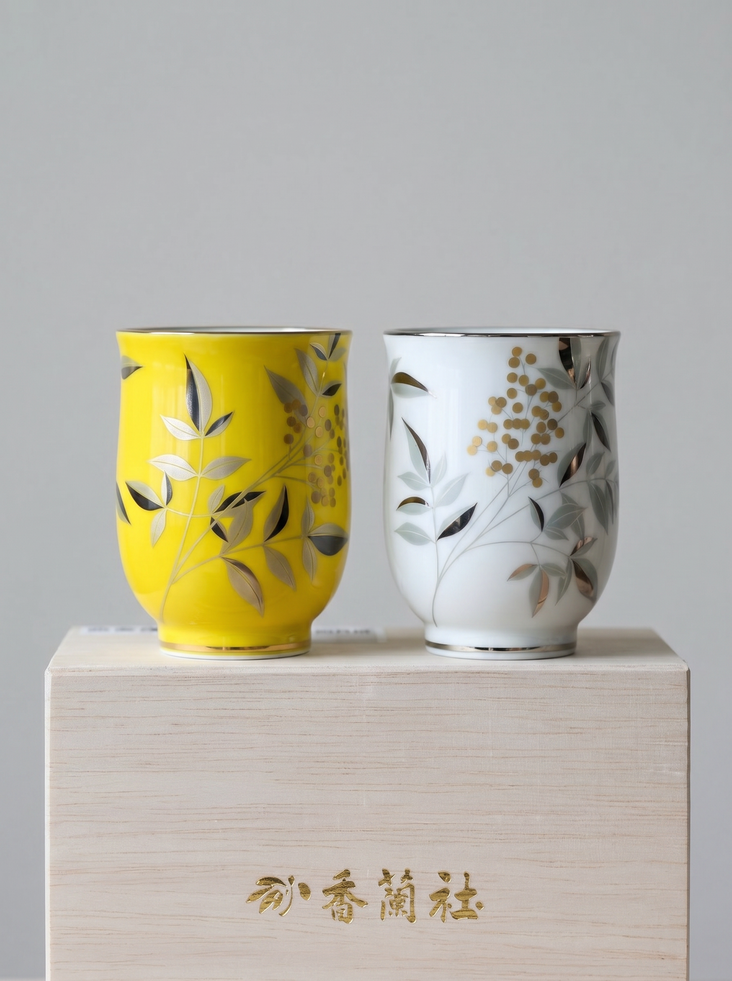 Two ceramic cups, one yellow and one white, with floral designs on a gift box against a grey background.