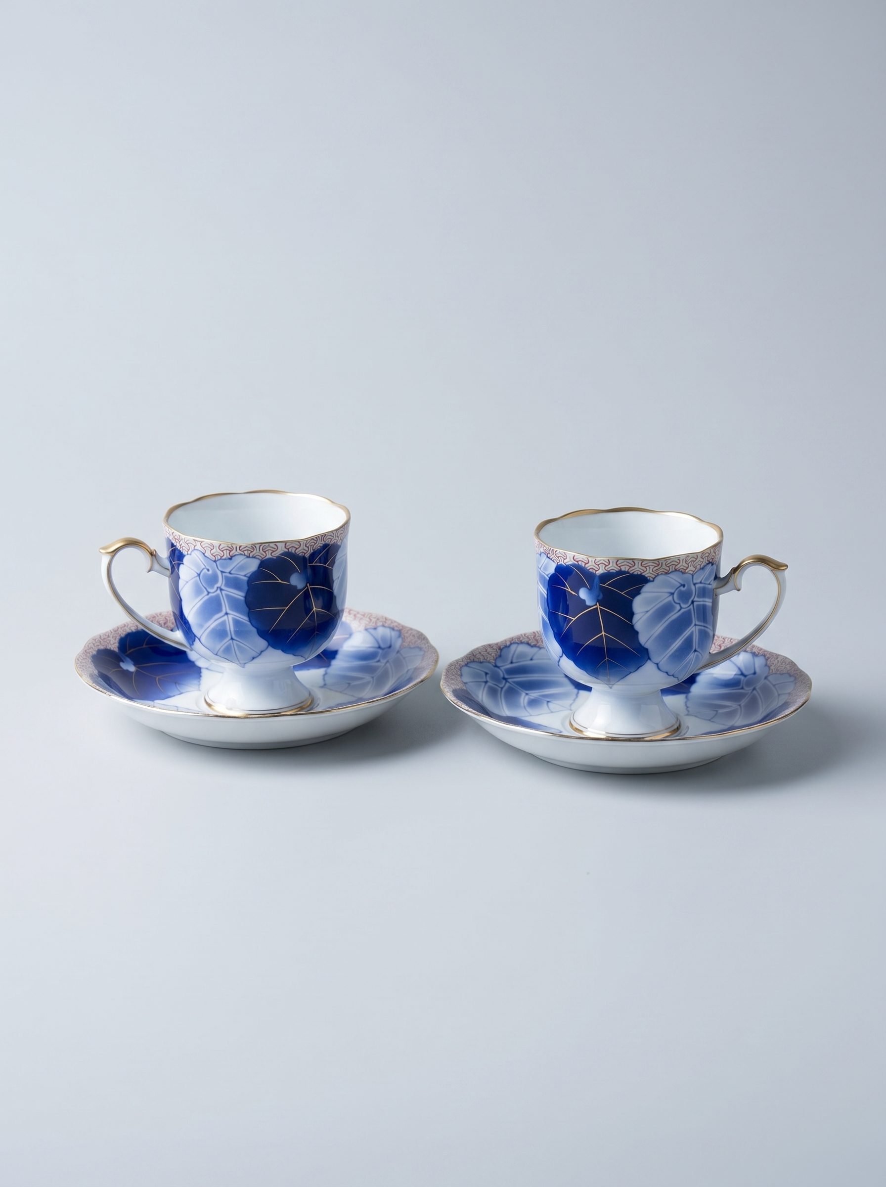 Two ceramic tea cups with saucers featuring blue floral patterns on a light gray background