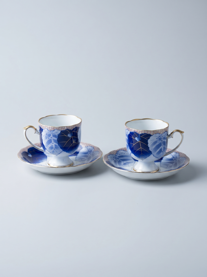 Two ceramic tea cups with saucers featuring blue floral patterns on a light gray background