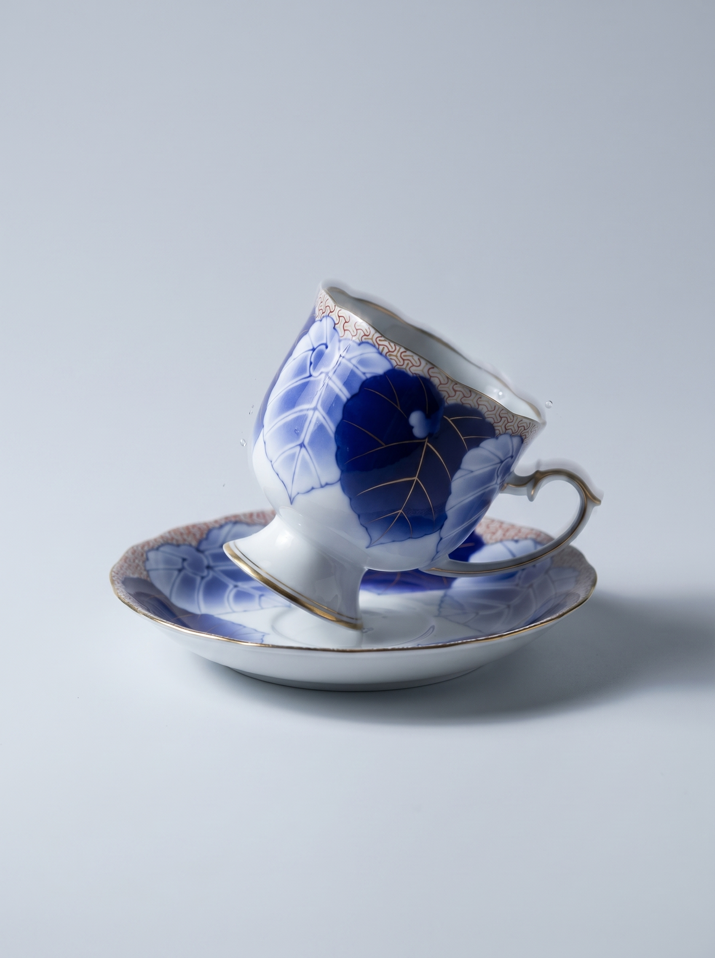 Ceramic teacup and saucer with blue floral design on a light gray background
