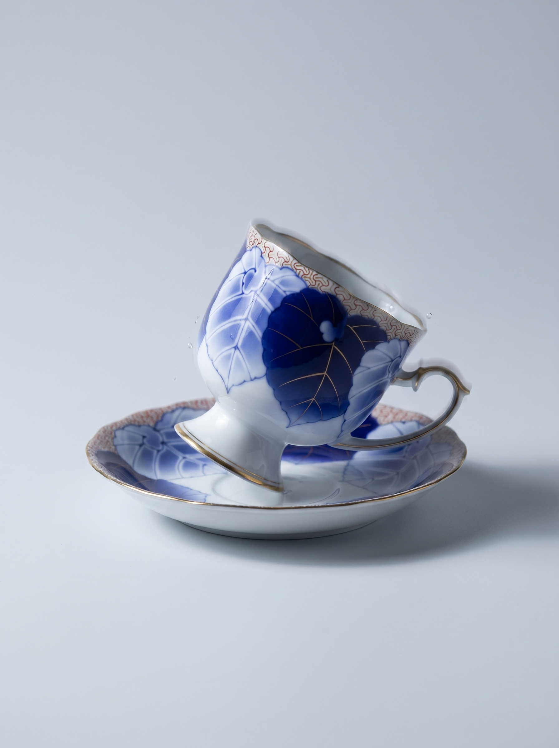 Ceramic teacup and saucer with blue floral design on a light gray background
