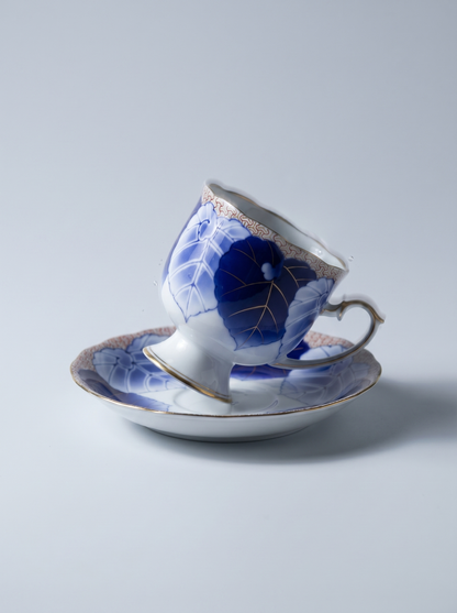 Ceramic teacup and saucer with blue floral design on a light gray background