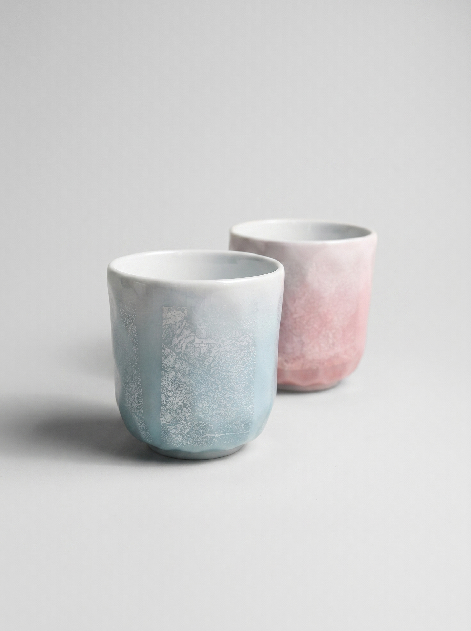Two ceramic cups with ginsai finish, one light blue and one pink, on a gray background