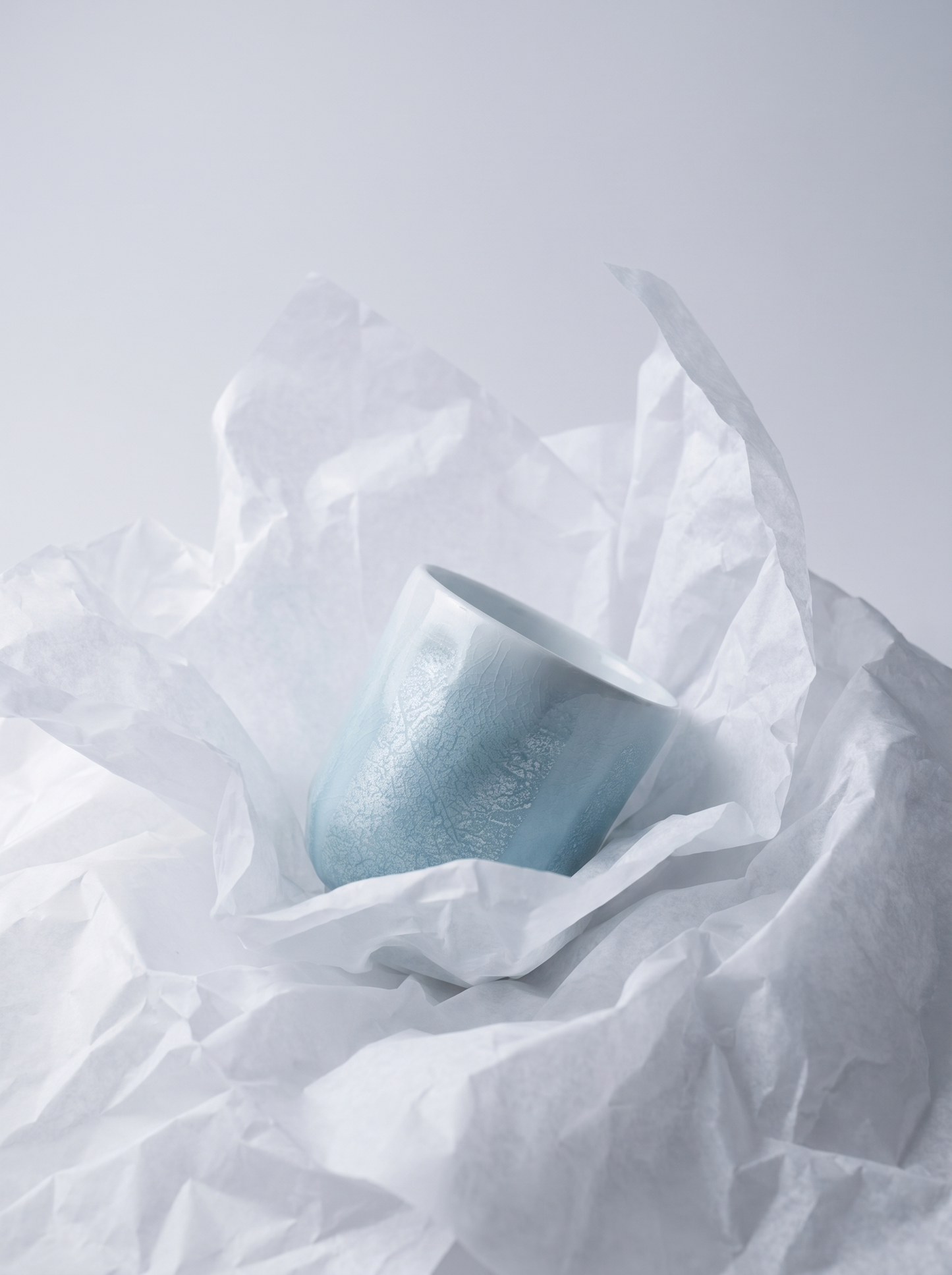 Light blue teacup inside crumpled white paper on a light gray background