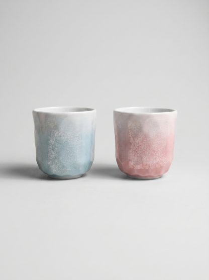 Two Japanese kutani ceramic cups with ginsai finish, one blue and one pink, on a light gray background