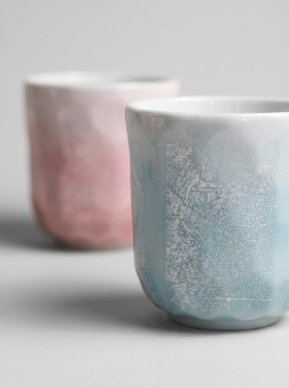 Two ceramic cups with ginsai finish surfaces on a light gray background