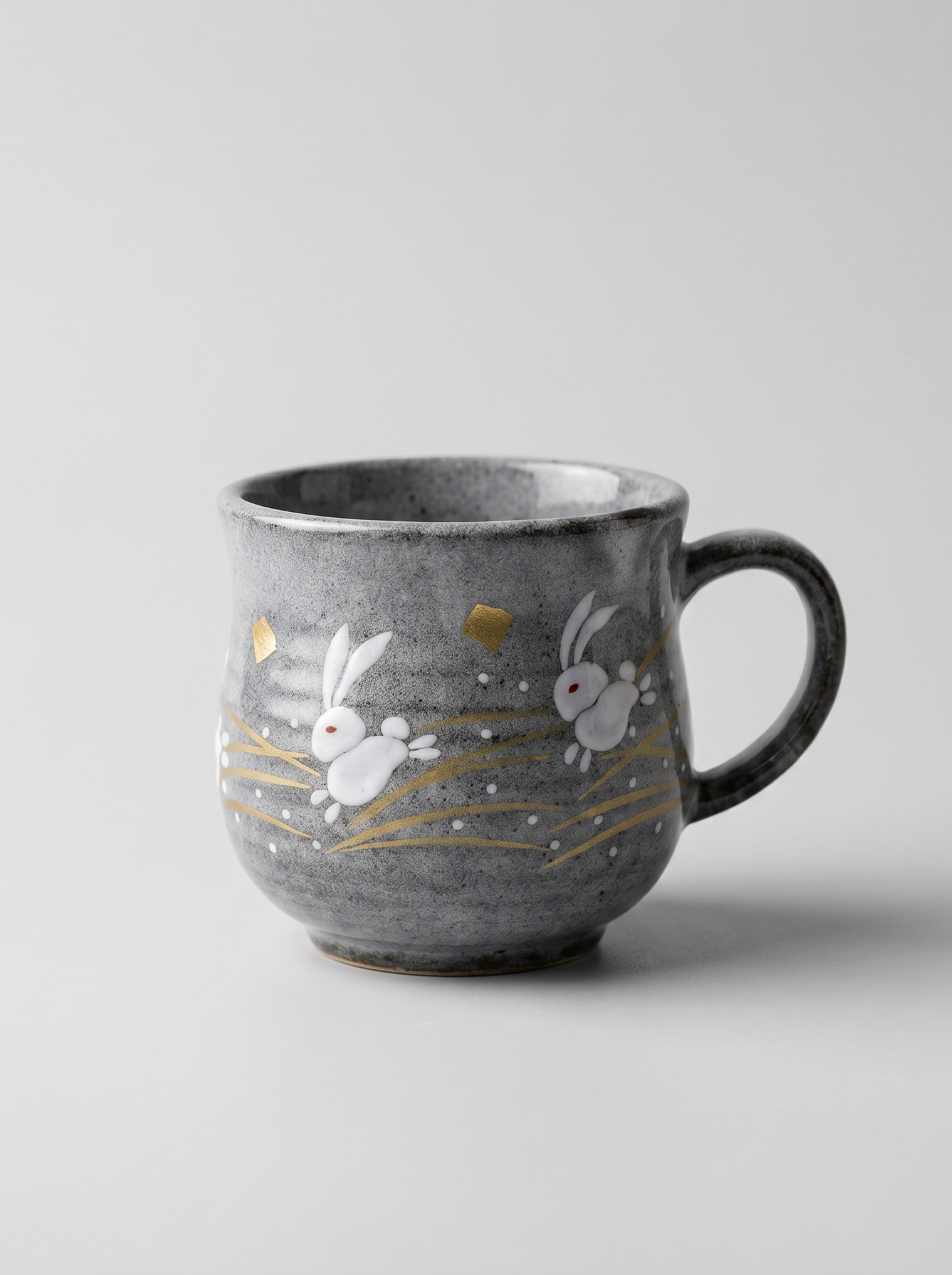 Japanese kutani ceramic teacup with a short handle with golden moon and rabbit design for tea, matcha latte, coffee, hojicha on a light grey background, front-facing