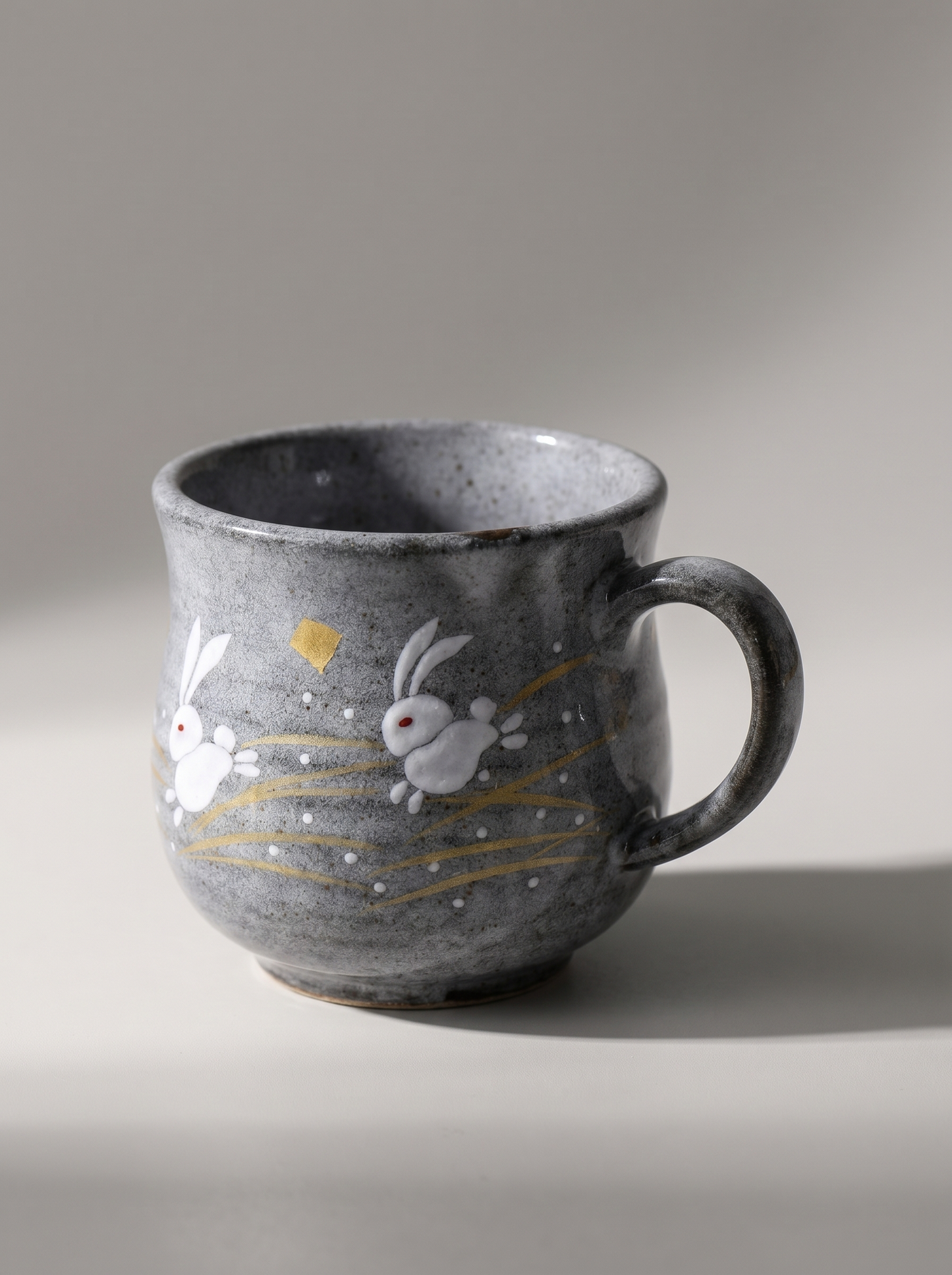 Gray ceramic mug with rabbit illustrations on a neutral background