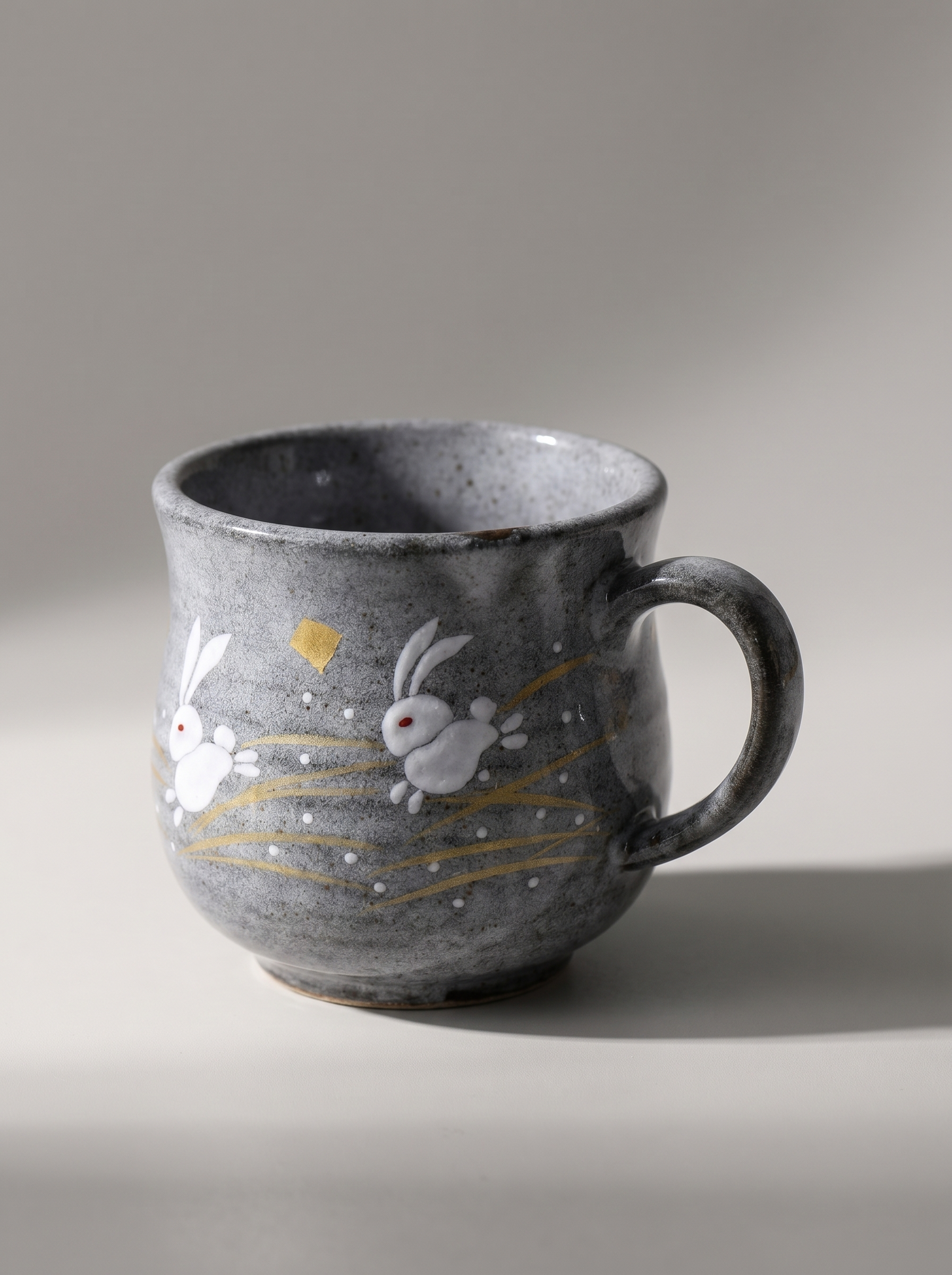 Gray ceramic mug with rabbit illustrations on a neutral background
