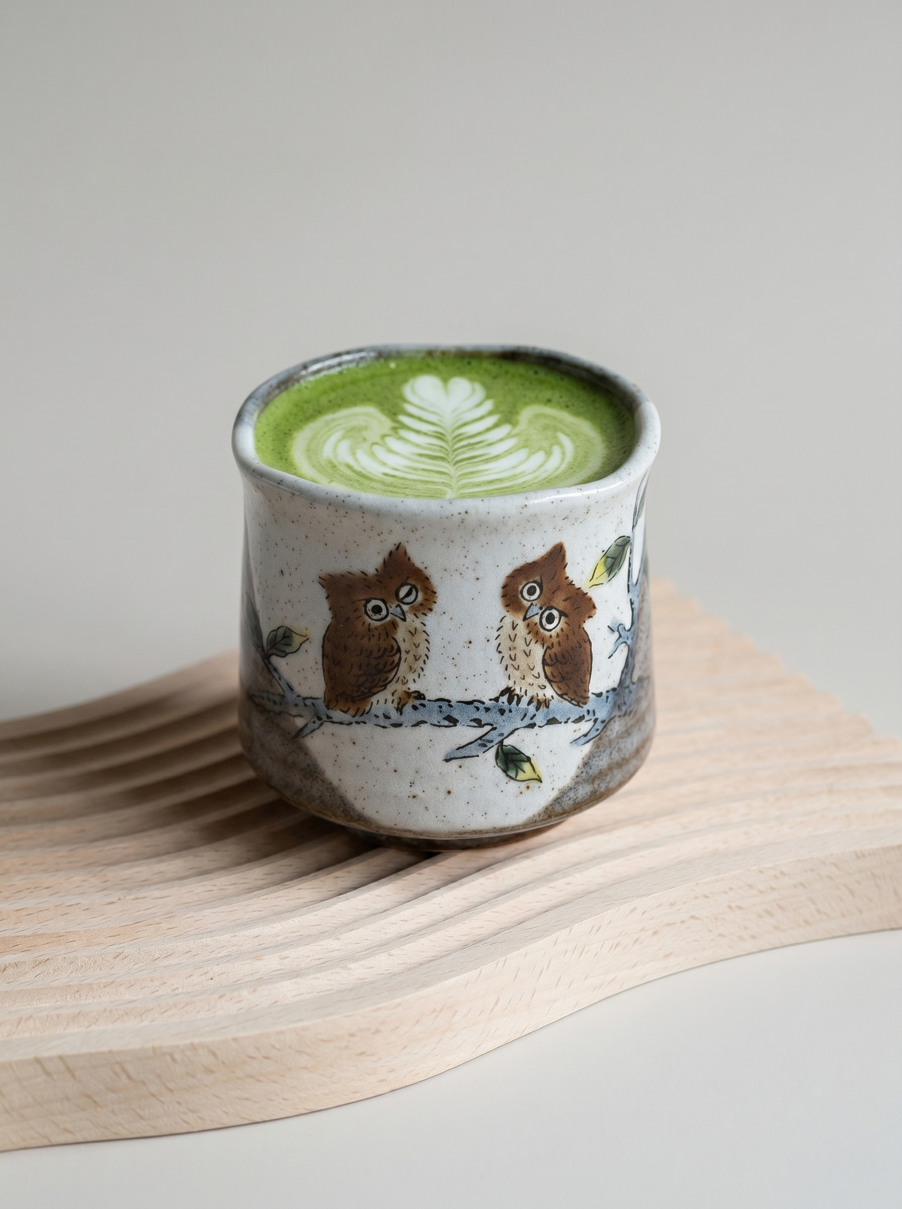 Ceramic cup with owl design filled with green matcha on a wooden surface.